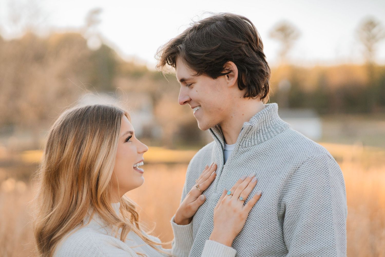 A couple shares an intimate moment while laughing together in a sunlit outdoor setting at golden hour.