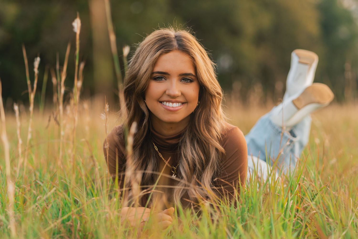 Person in casual attire lying in tall grass during golden hour sunset photography session in nature.