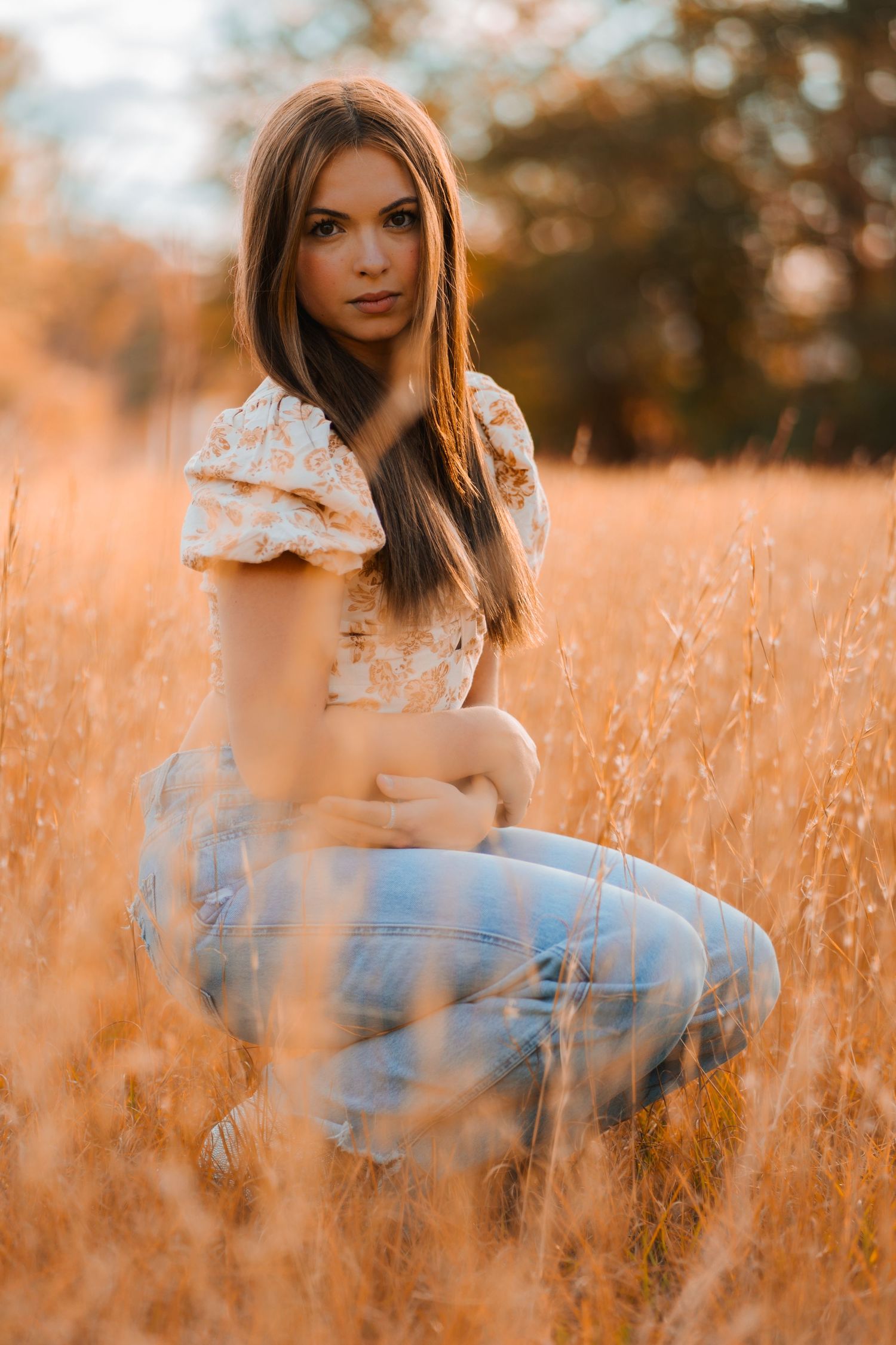 A portrait in a golden wheat field at sunset showing a floral top and blue jeans against warm autumn colors.