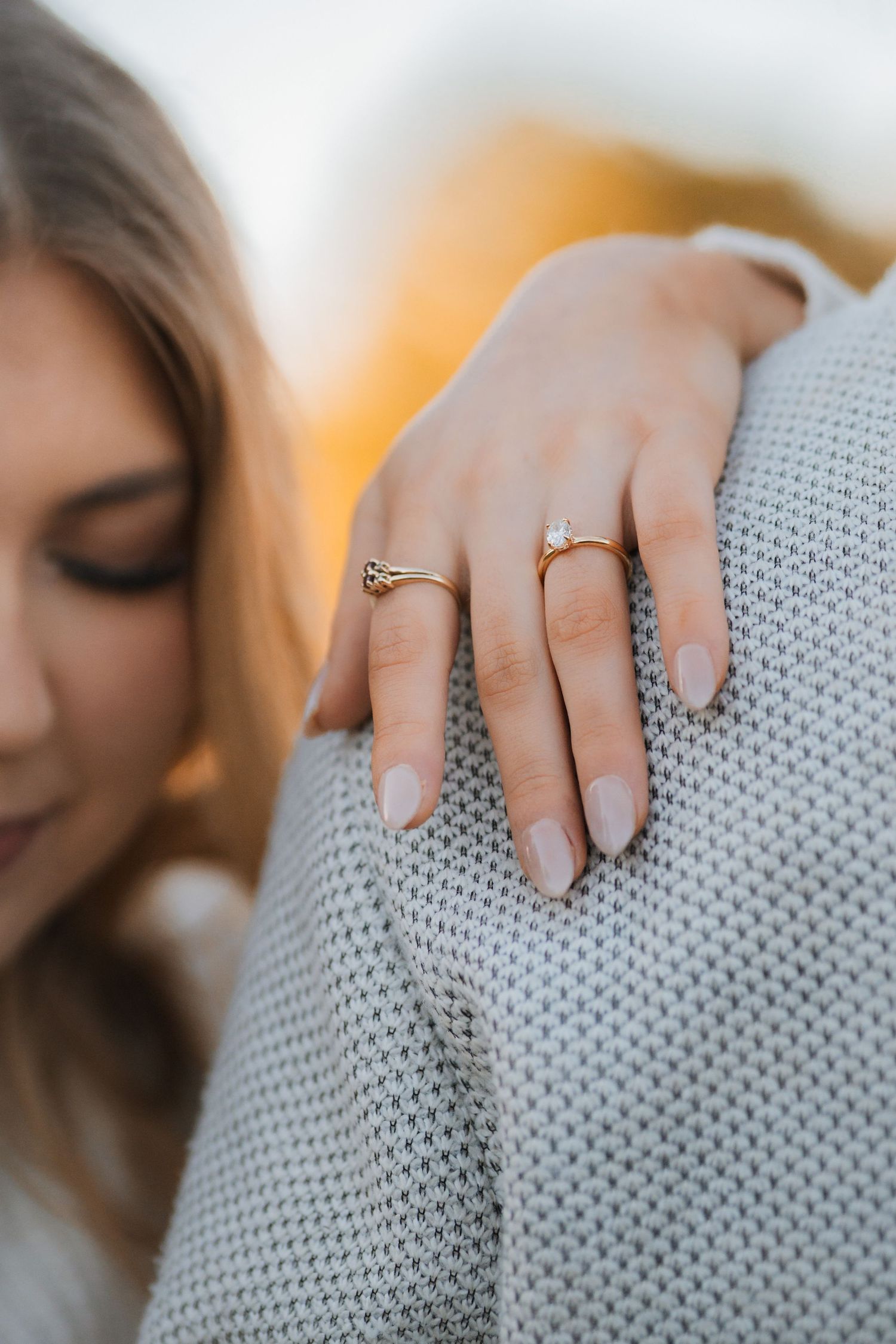 Close-up shot of hands wearing delicate rings resting on a soft gray textured knit sweater.