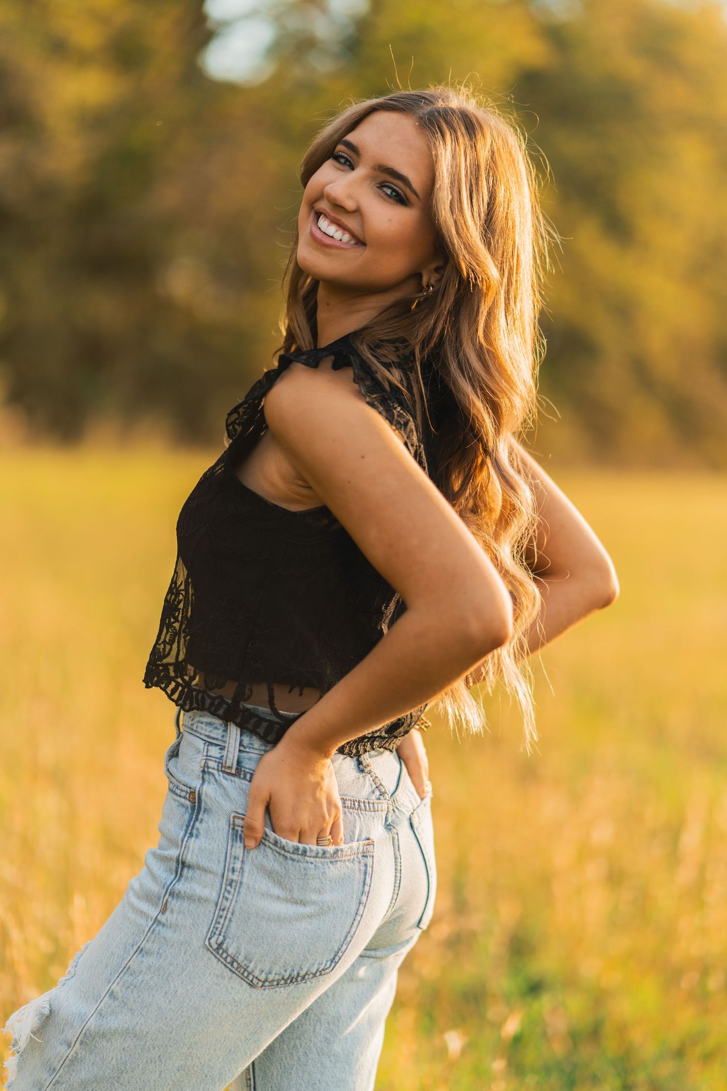 Golden sunlit portrait of someone wearing a black lace top and light denim jeans in a summer meadow.