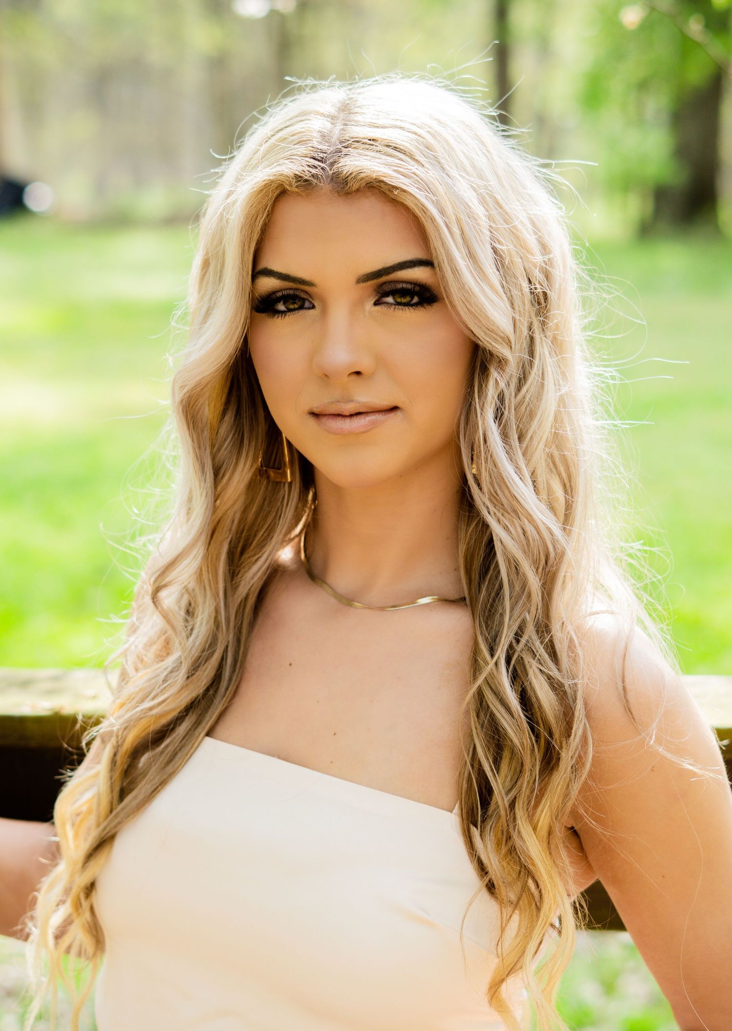 Portrait photo showing long wavy platinum blonde hair and natural makeup in an outdoor garden setting with soft lighting.