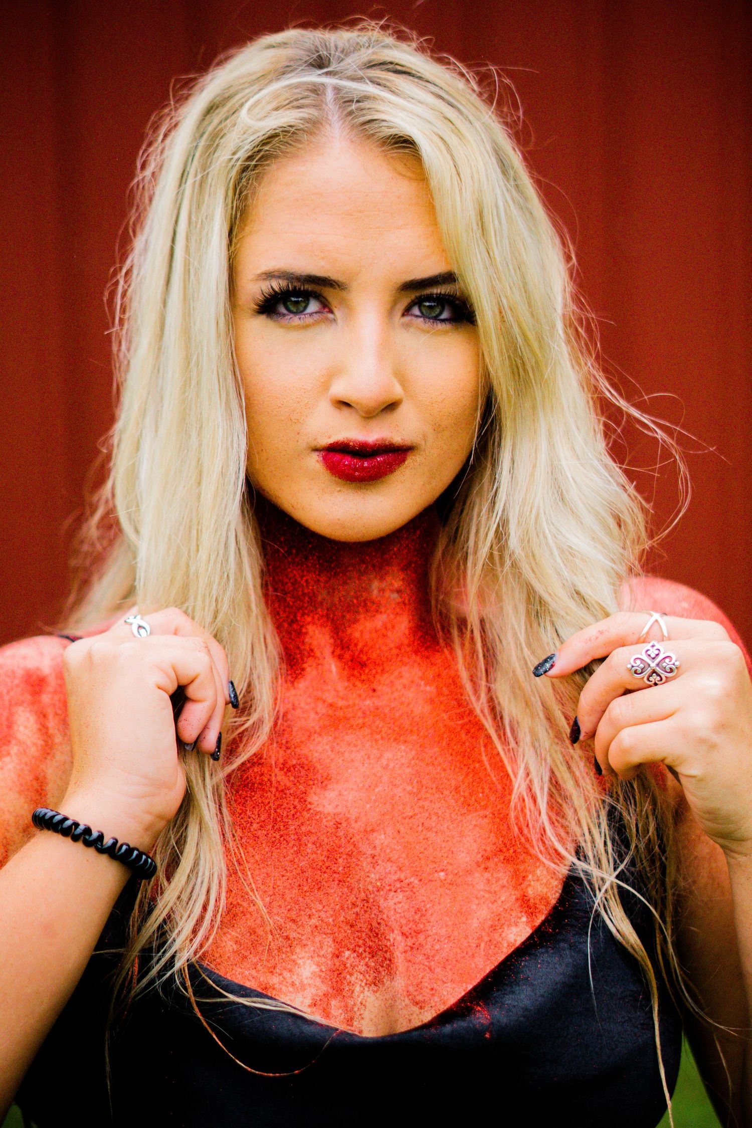 Portrait of a blonde woman in a black top with red velvet neckline detail wearing bright red lipstick.