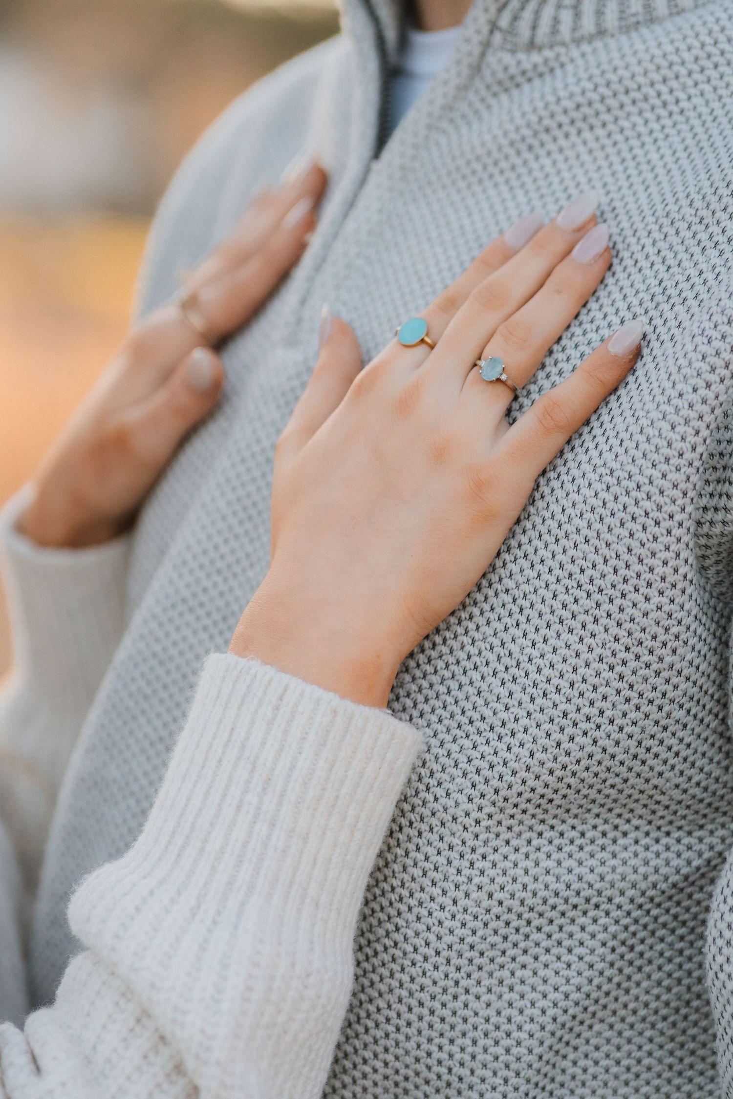 A delicate hand adorned with turquoise rings rests against a soft grey knit sweater.