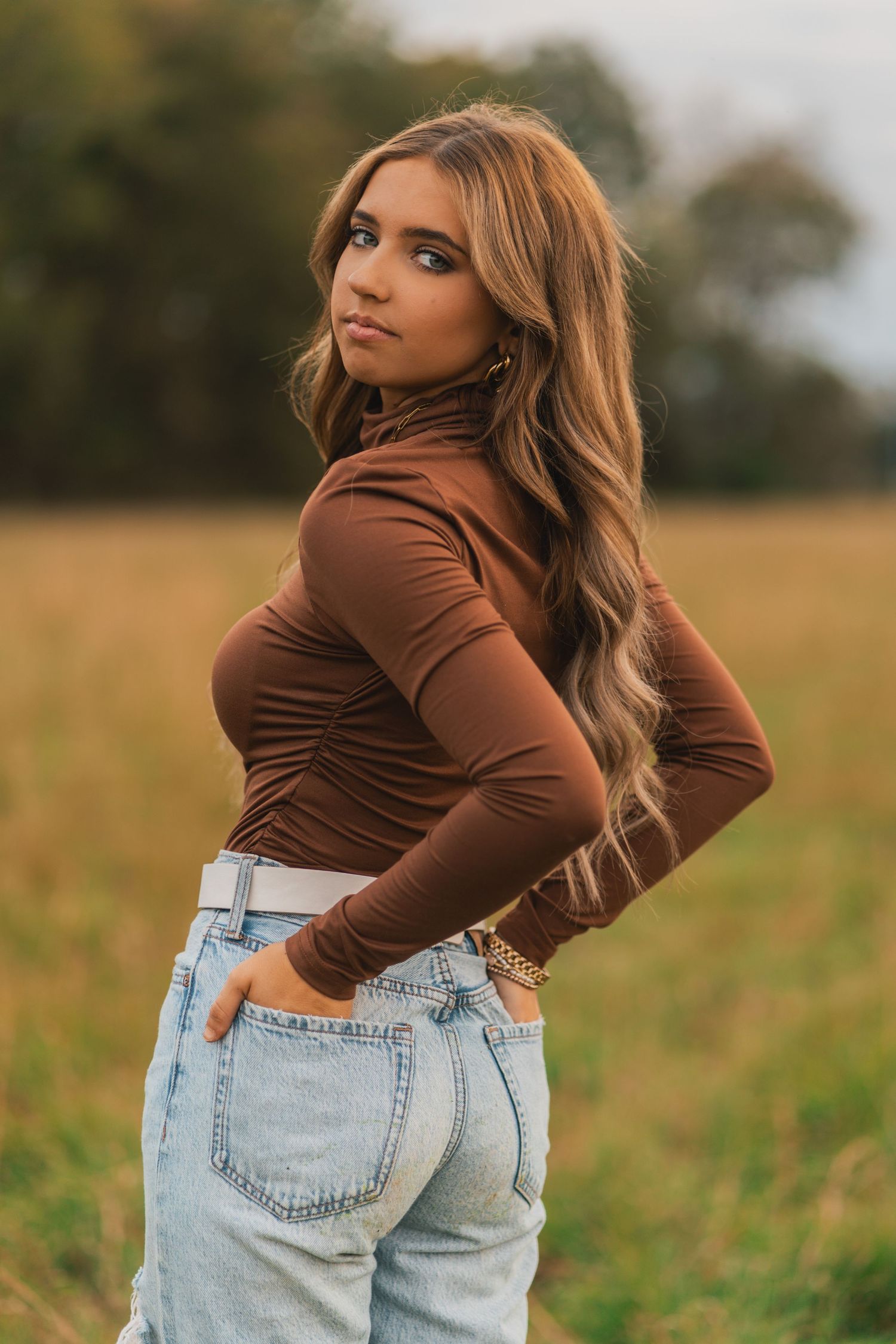 A stylish brown turtleneck top paired with light wash mom jeans in an autumn field setting at golden hour.