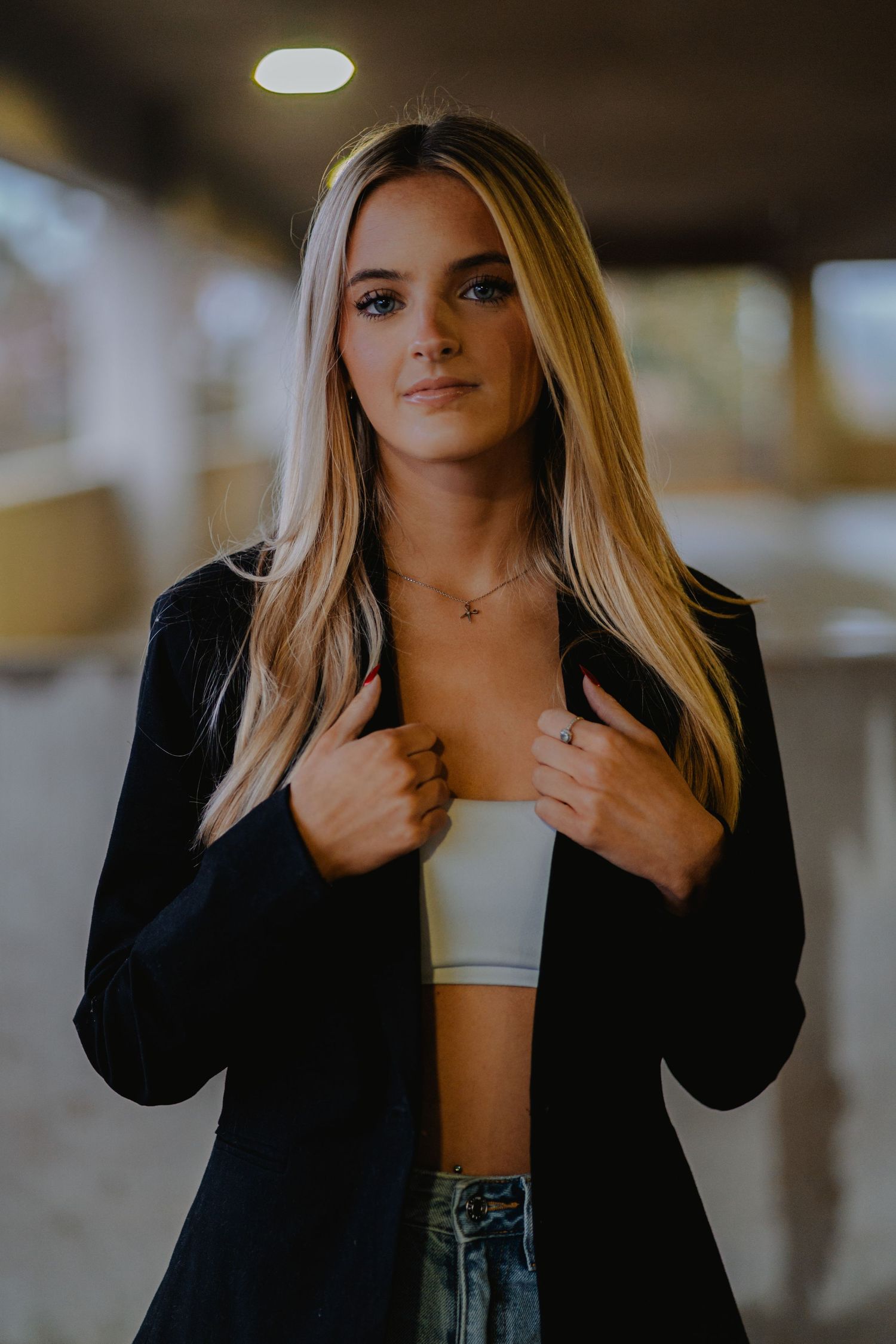Fashion model wearing black blazer with white crop top and denim in moody indoor lighting.