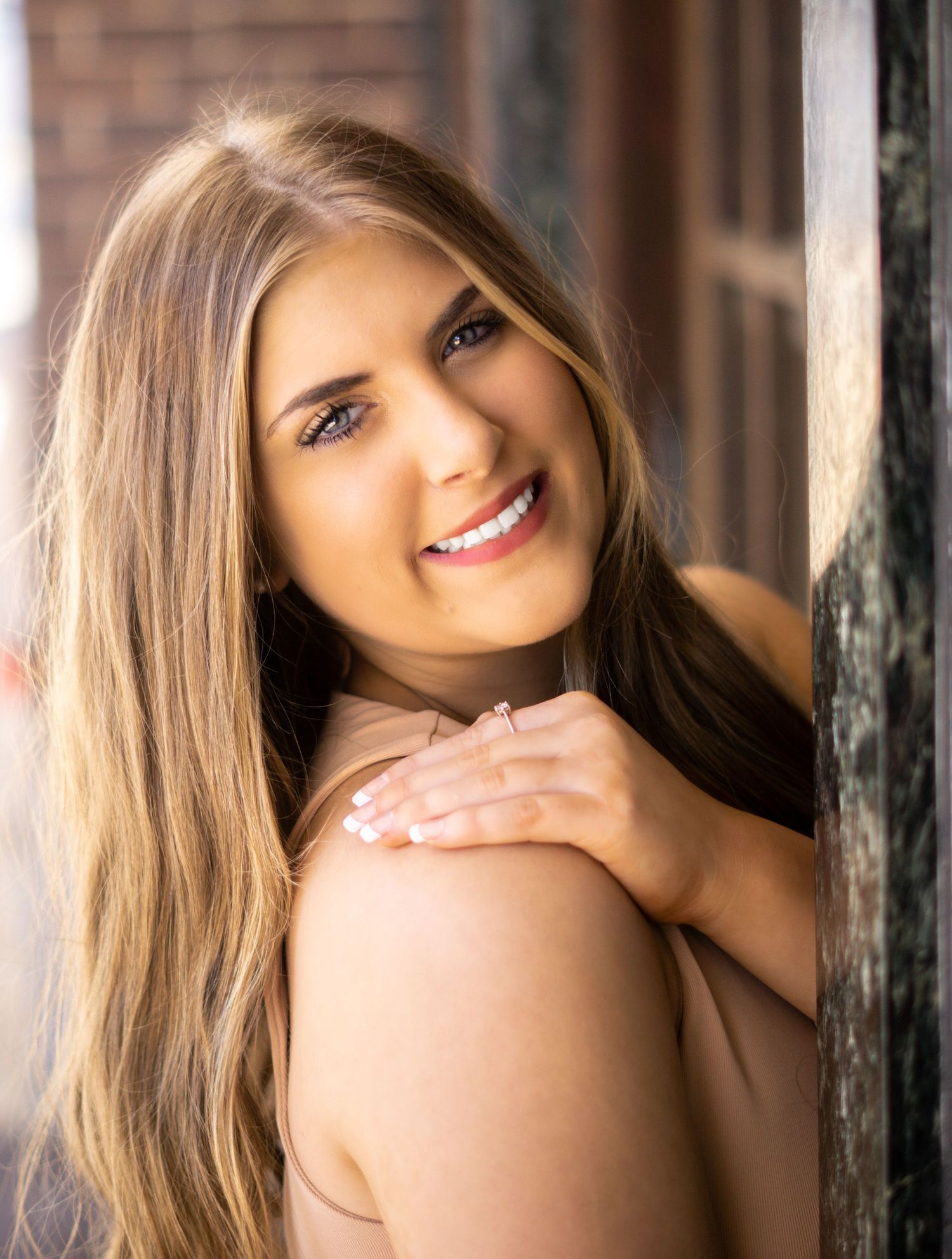 Portrait of a smiling woman with long blonde hair leaning against a wall in warm sunlight.
