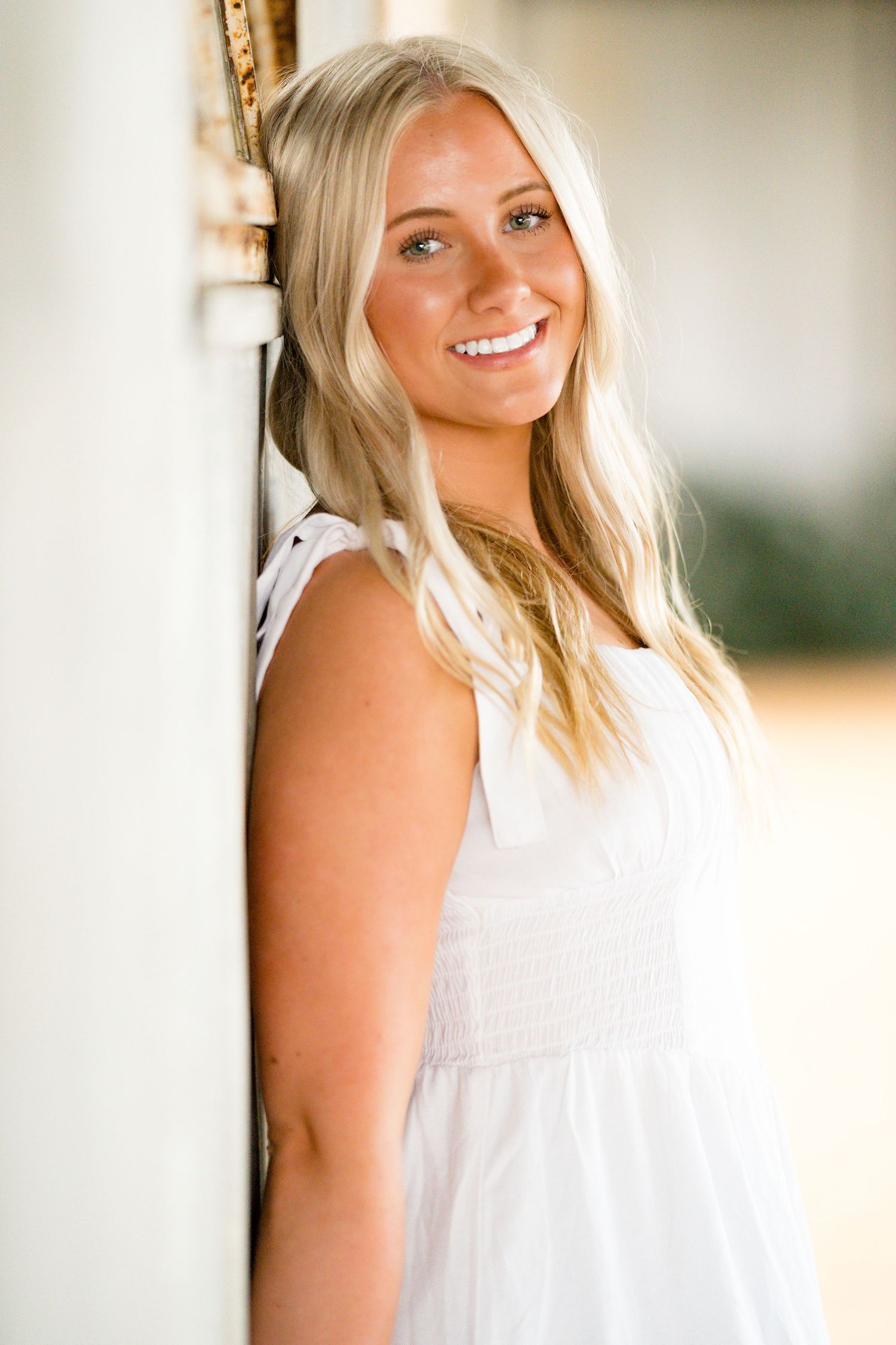 Portrait series of a person in a white sleeveless top smiling against a soft blurred background in warm lighting.