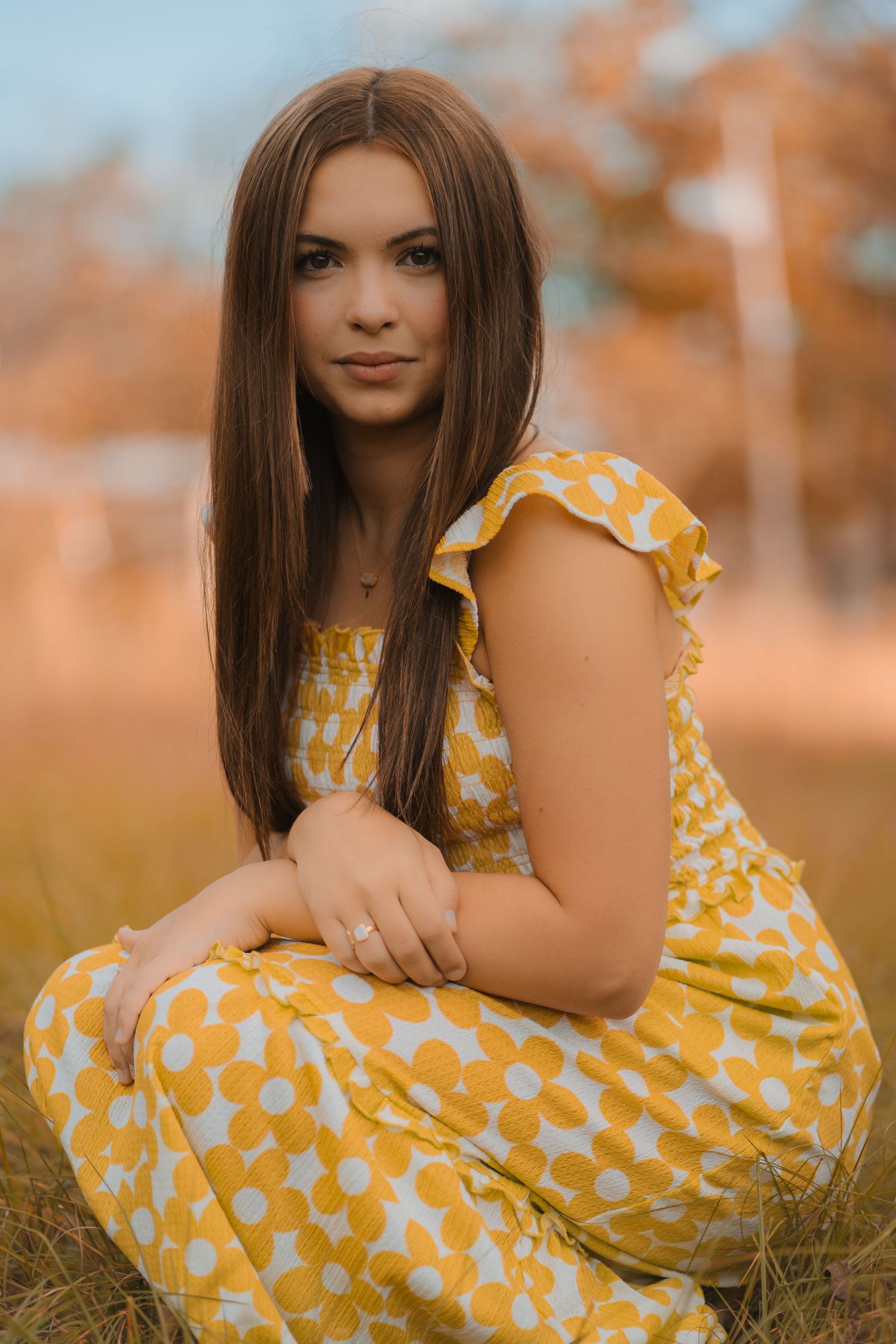 Portrait in a yellow polka dot dress with ruffled sleeves sitting in autumn field during golden hour.