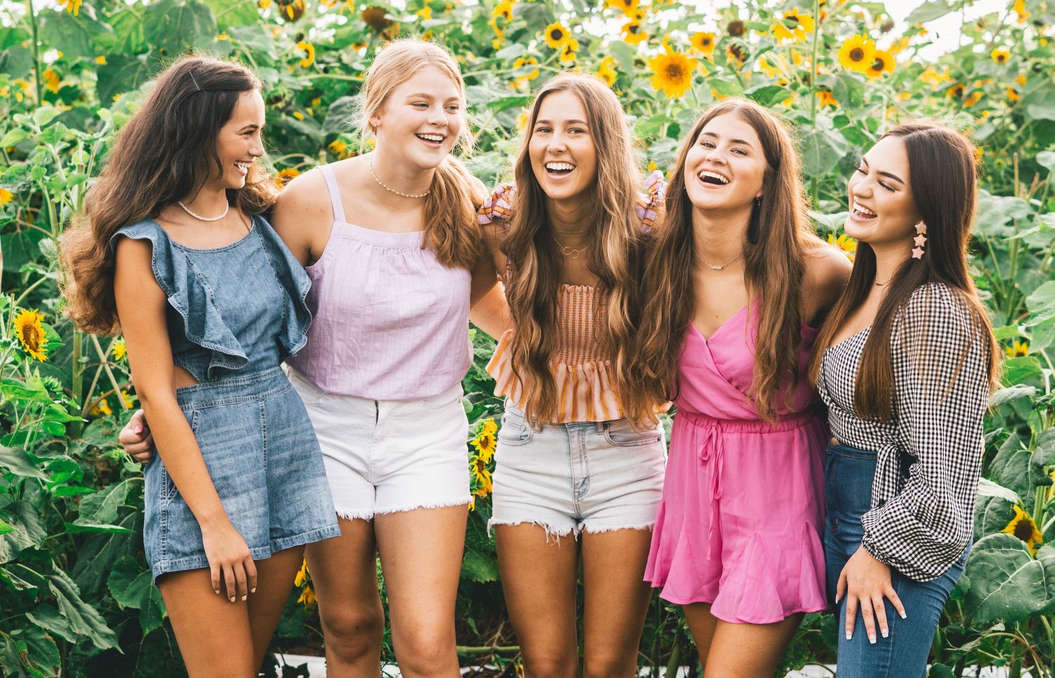 Group of five friends laugh together in a vibrant sunflower field on a bright summer day.