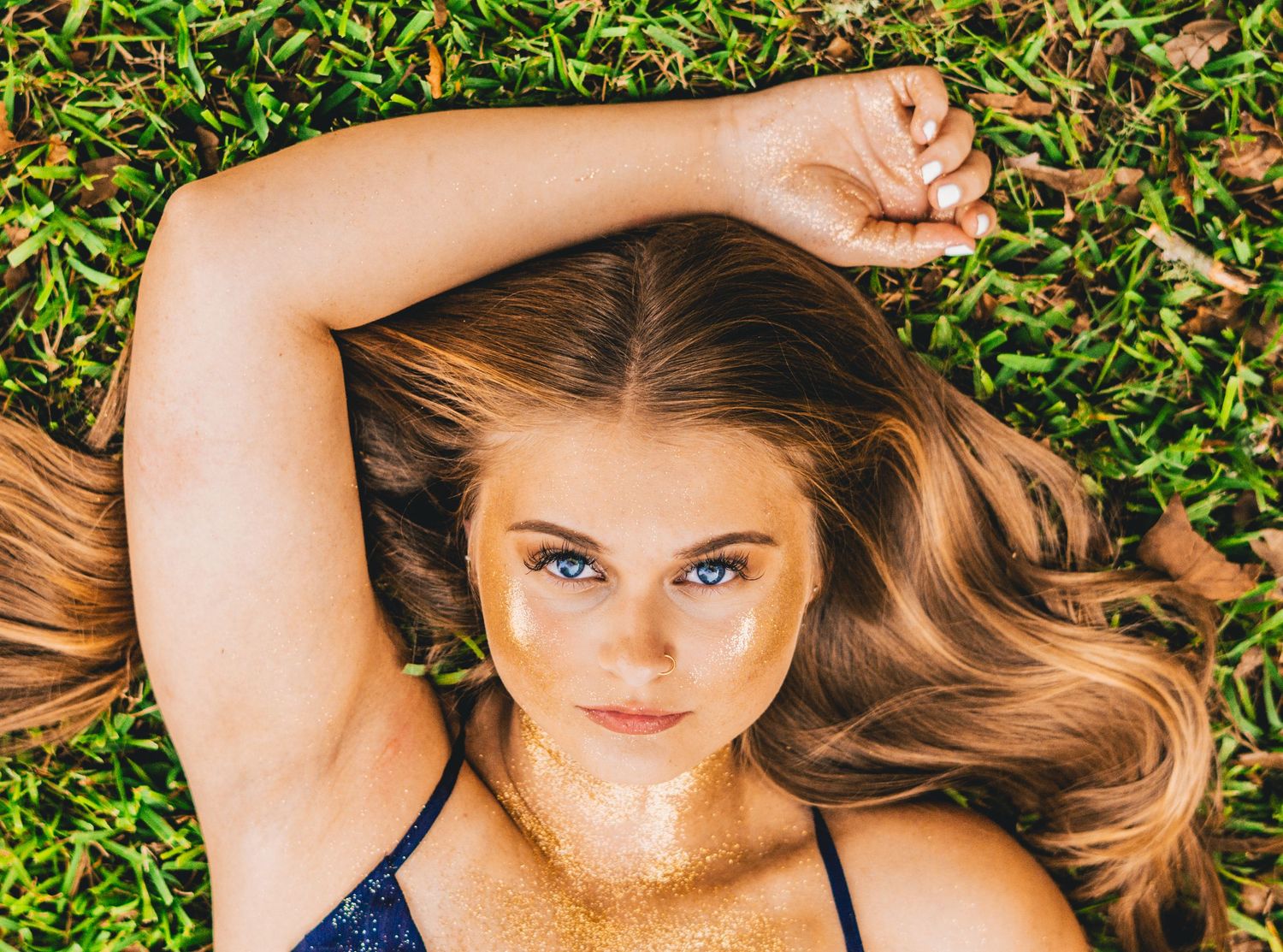 A portrait shot of someone lying in grass with long brown hair spread out and arm raised overhead.