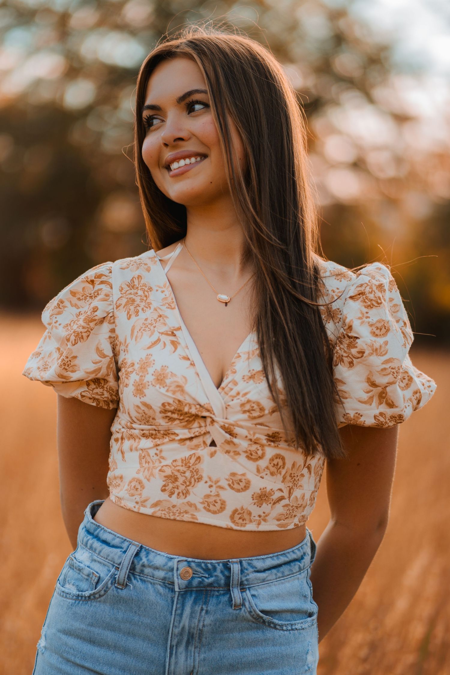 Golden hour portrait showing someone in a floral crop top with puff sleeves and high-waisted jeans in warm autumn lighting.