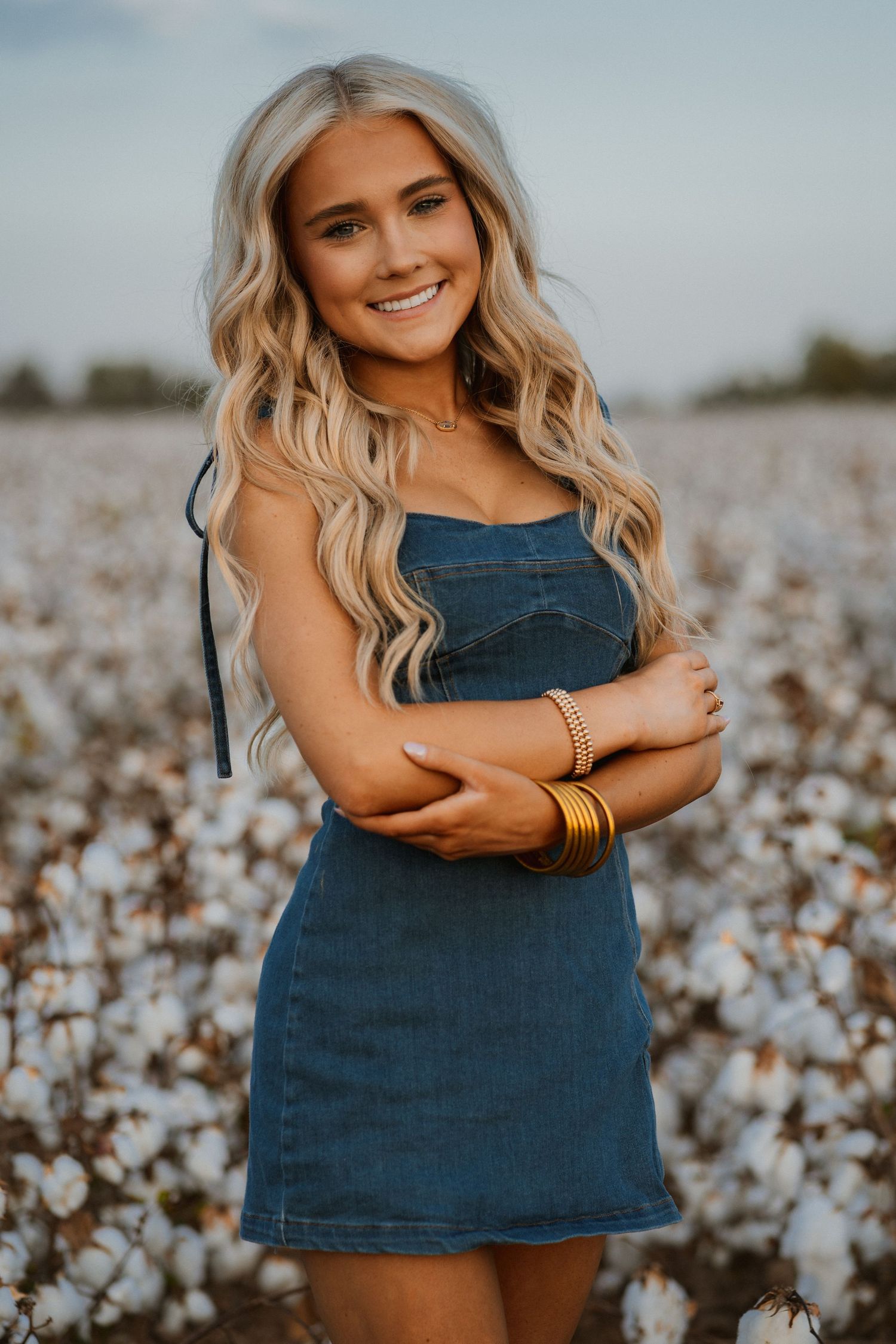 A casual summer portrait in a denim dress standing in a cotton field at golden hour.