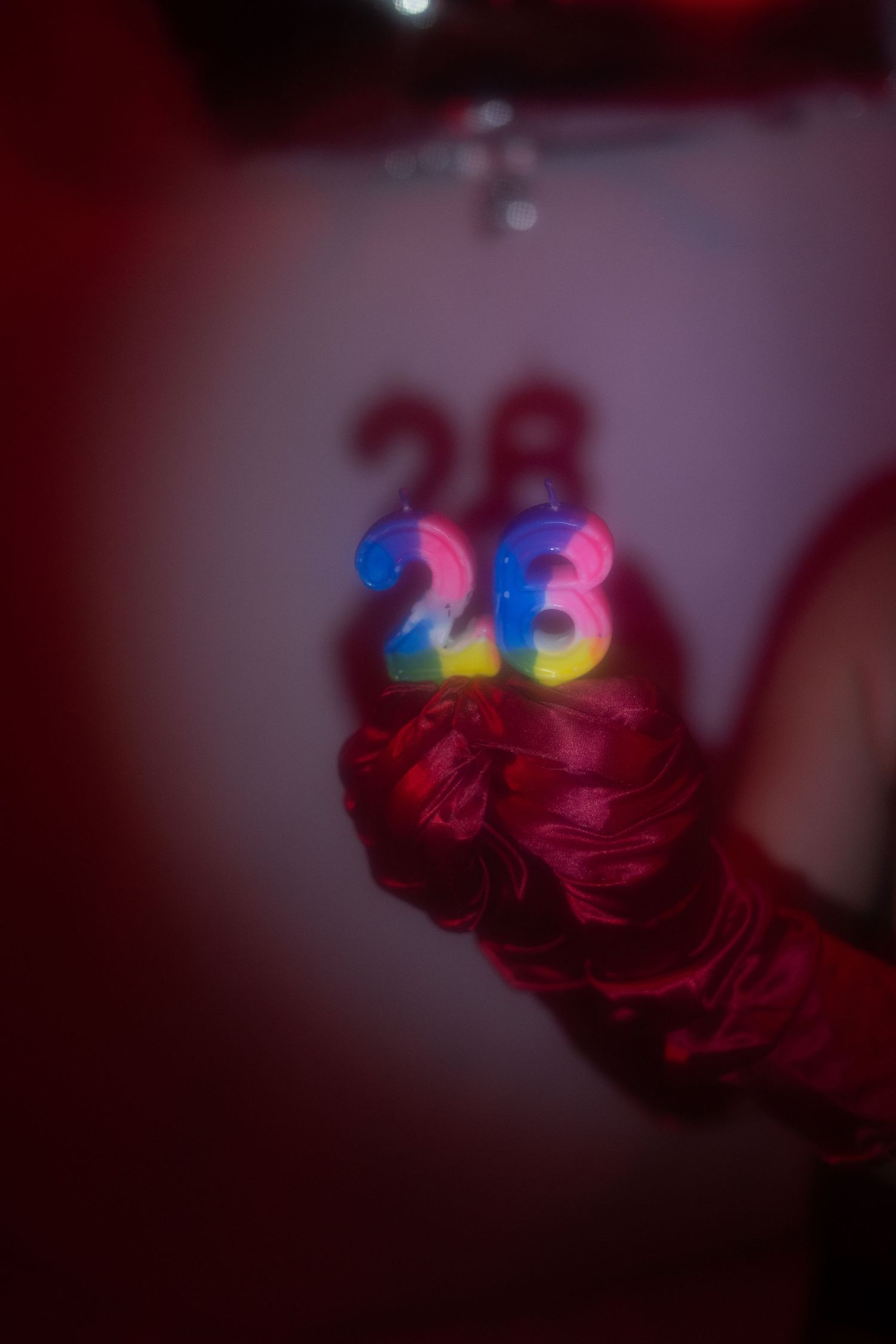 Red gloved hand holding colorful number 23 birthday candles in dim red light.