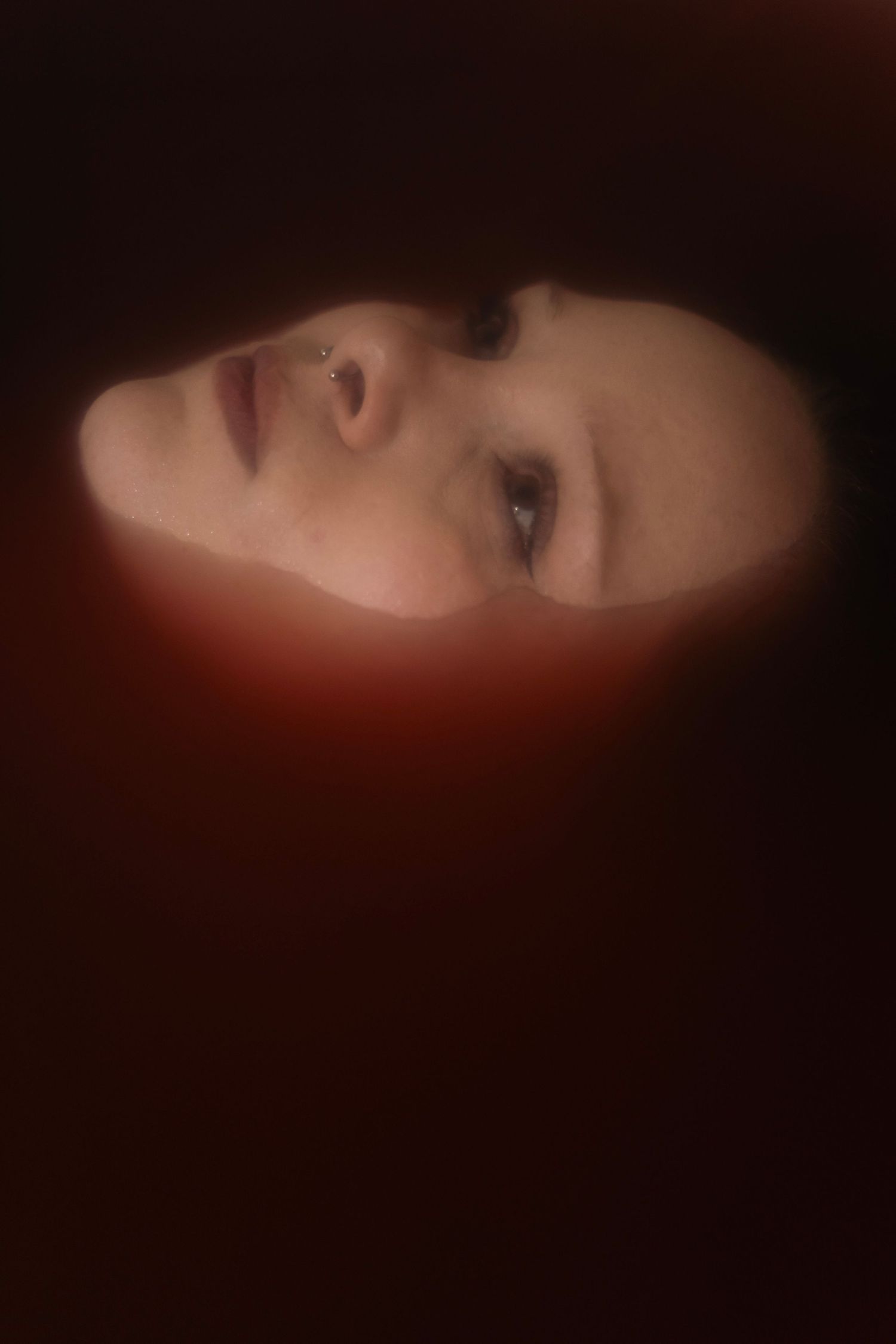 Close-up of a woman's face illuminated by red light in dark setting.