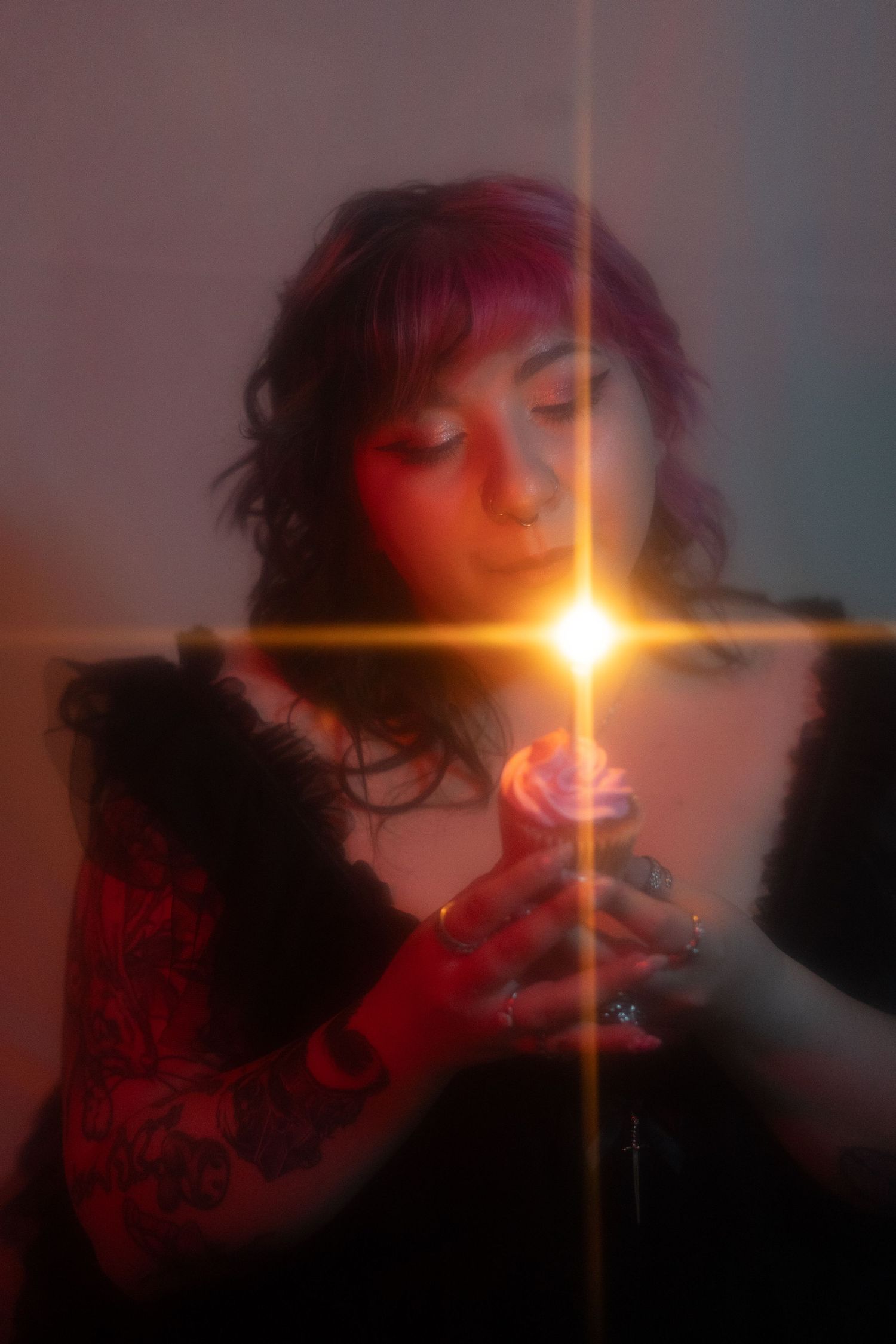 Woman with purple hair holding a glowing pink rose with lens flare effect in soft lighting.