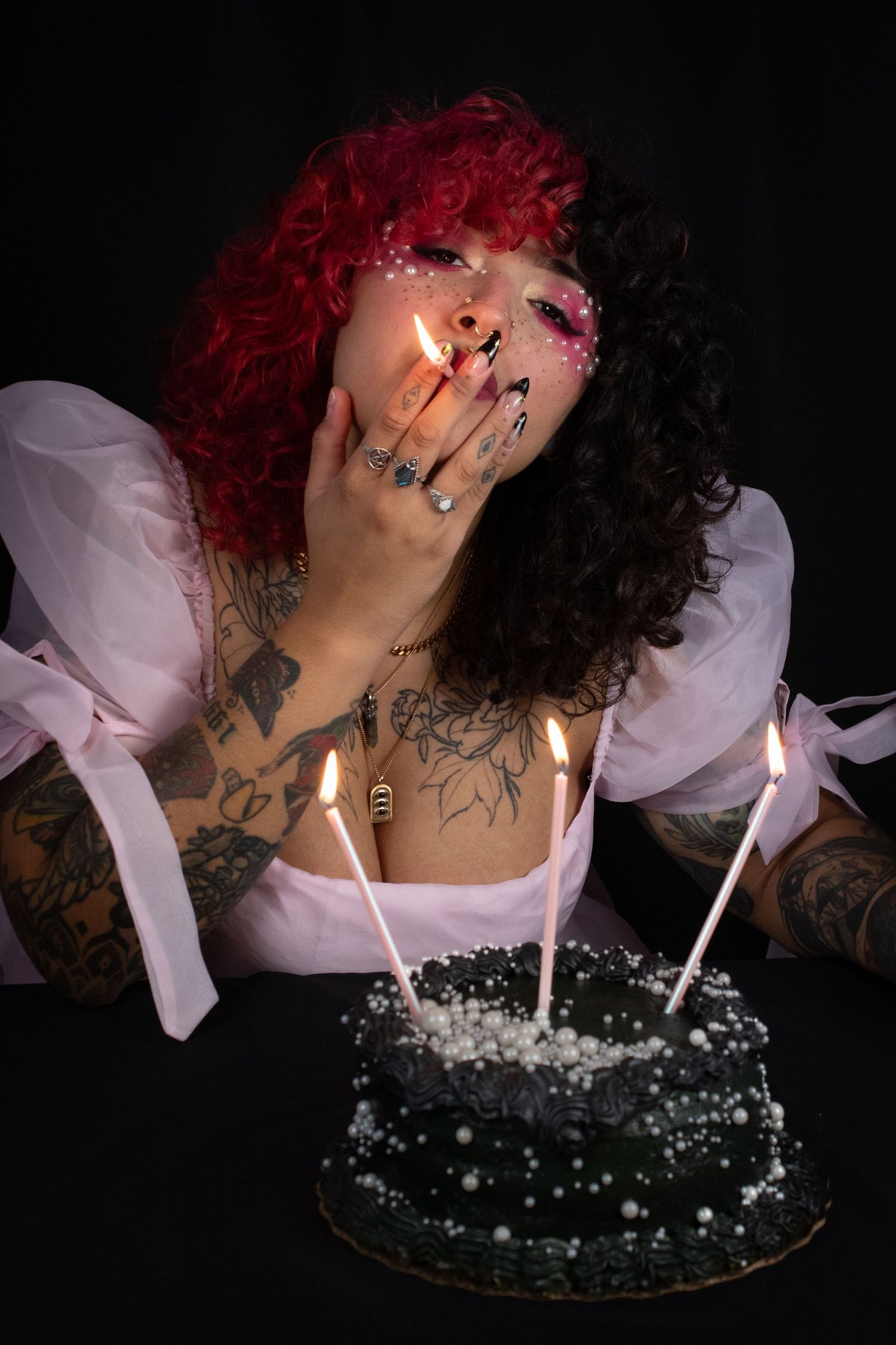 Woman with red and black split-dyed hair lights candles on dark birthday cake.