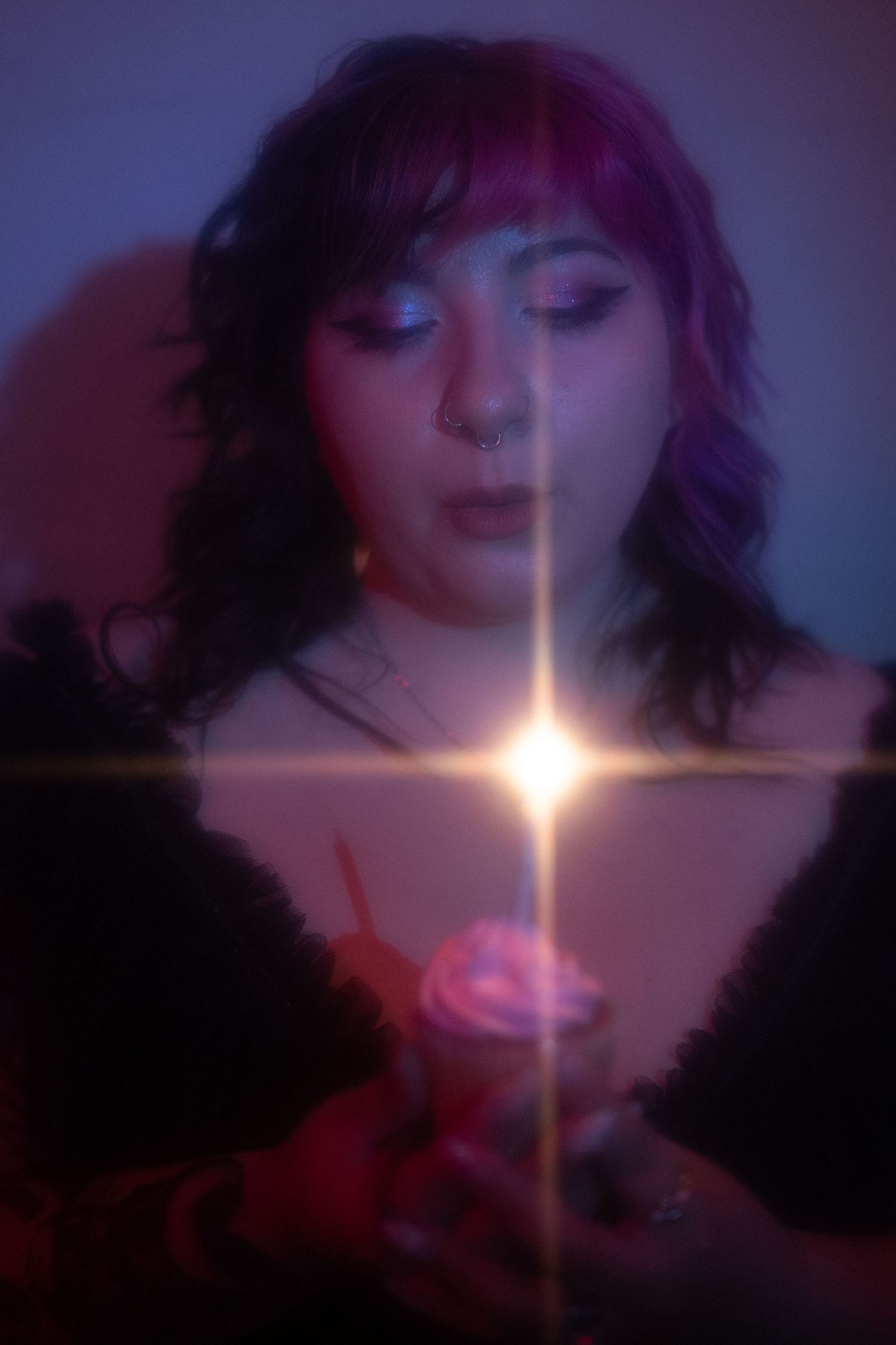 Person with purple hair holding a glowing candle in moody blue and pink light.