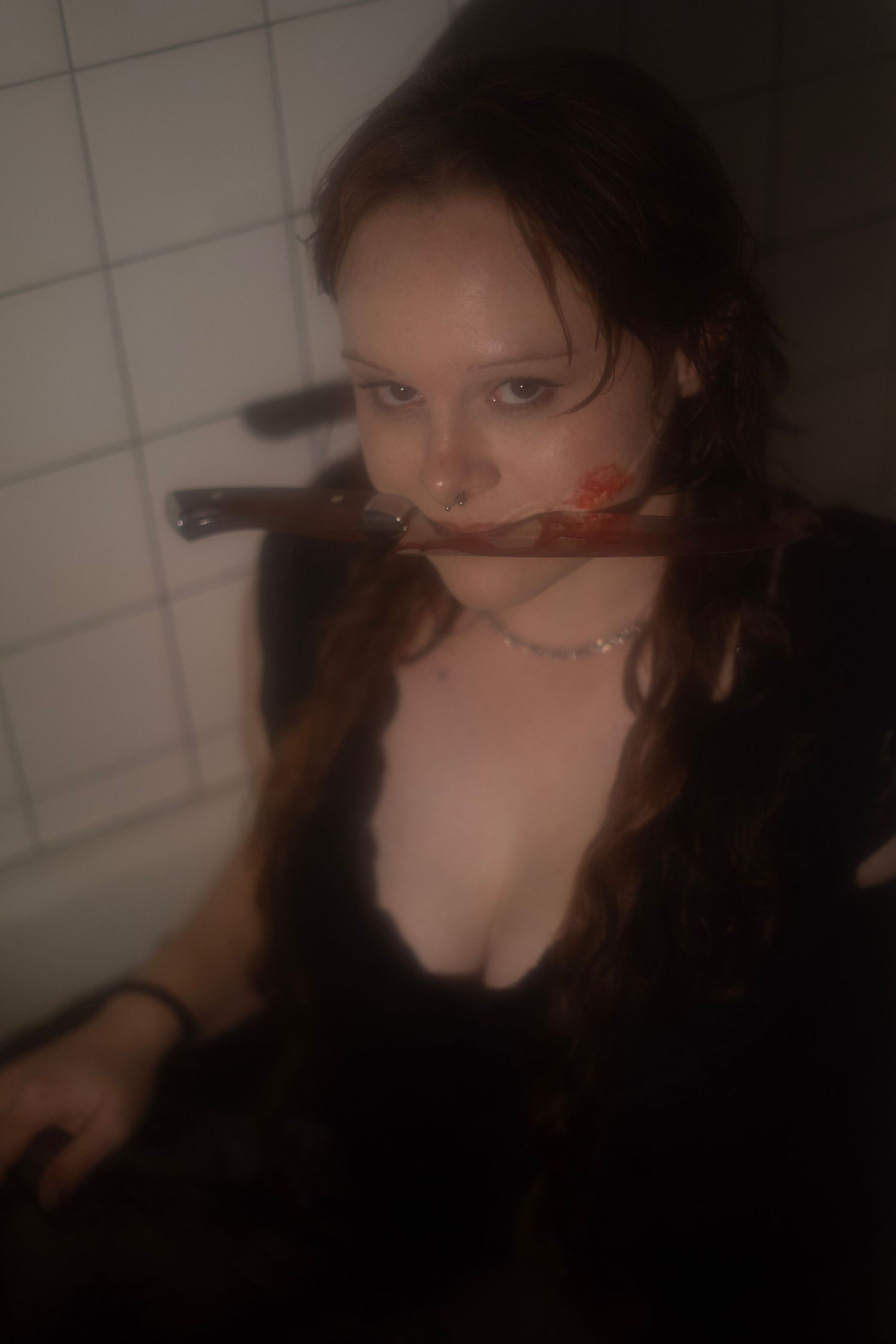 Woman with braids holding a knife in her mouth in a dark horror-themed photo.