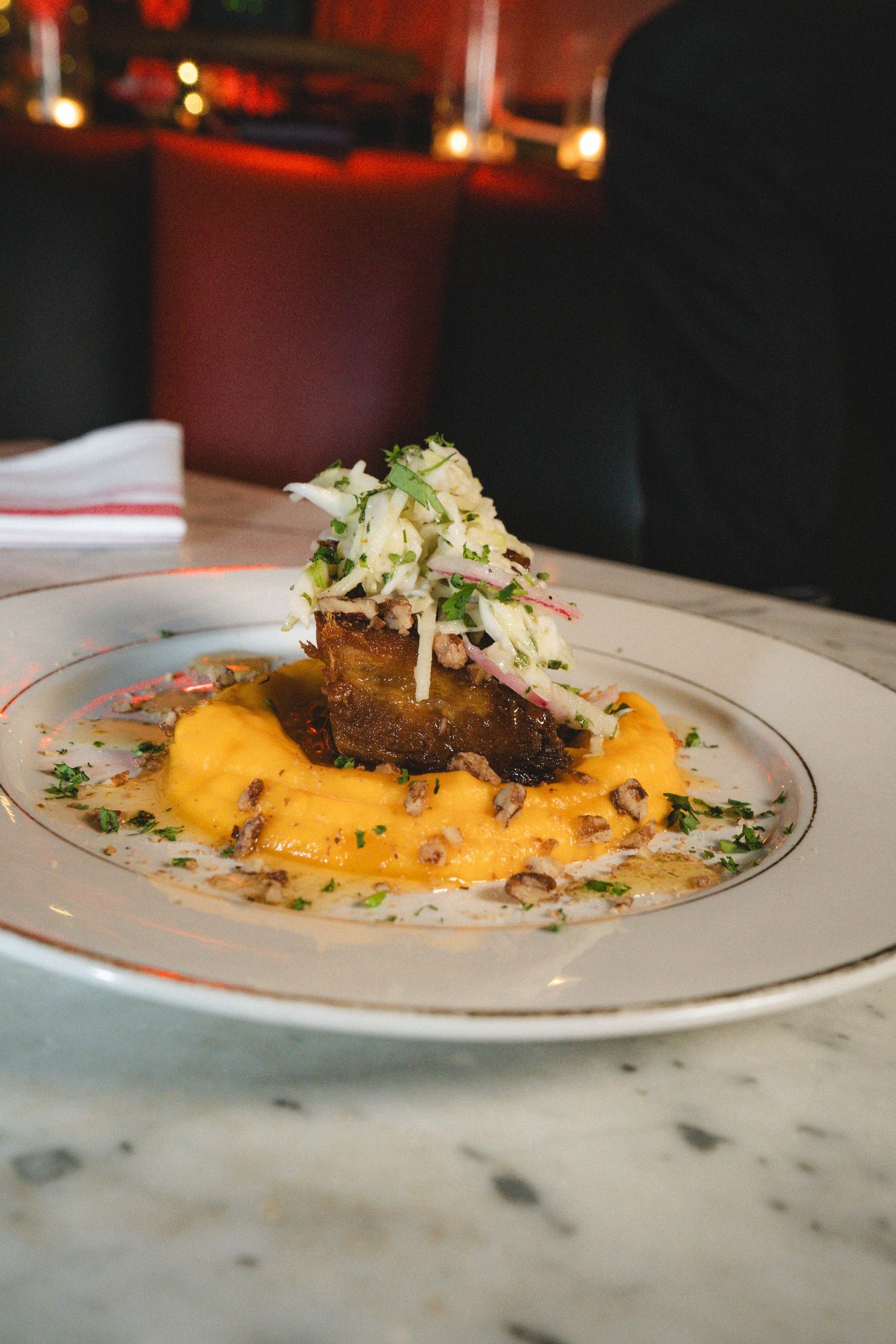 Gourmet braised meat dish with creamy orange sauce and fresh fennel slaw on white plate at restaurant.