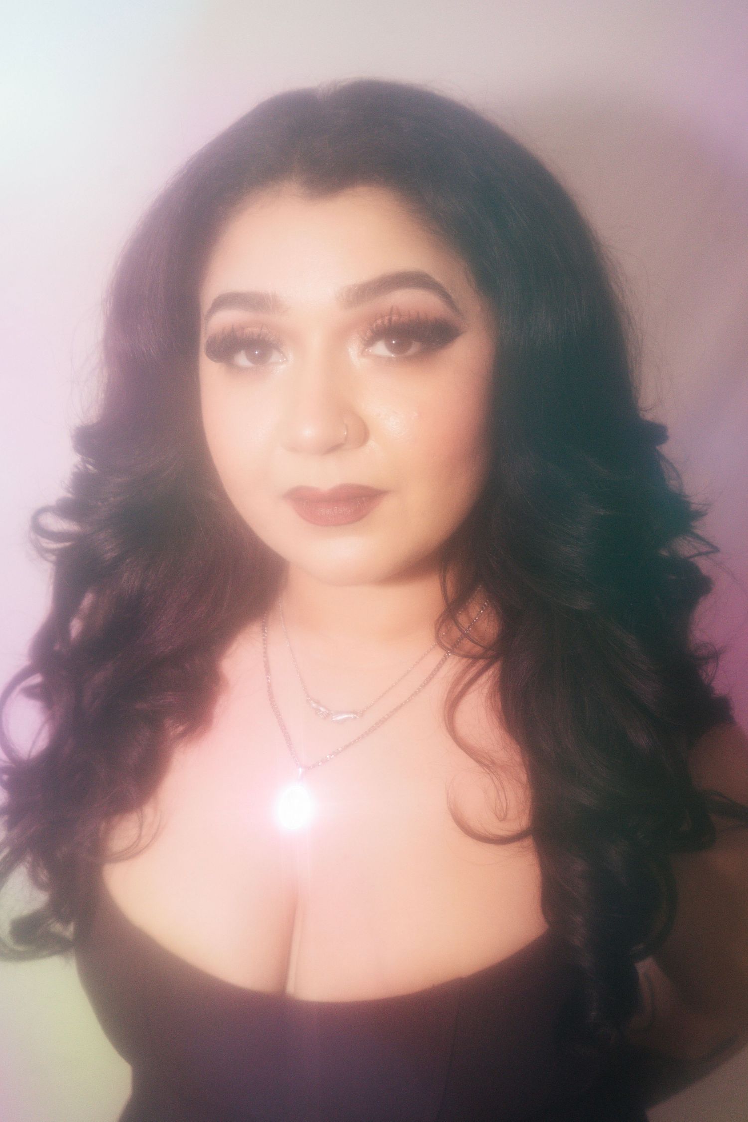 A woman with voluminous dark curly hair wearing a black top and layered necklaces.