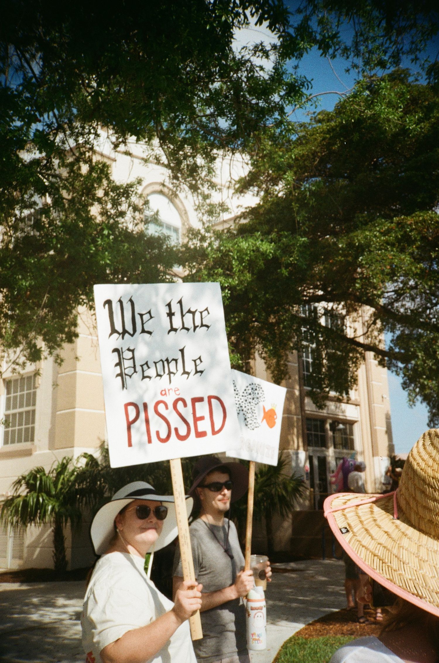 Woman holds 'We the People are PISSED' protest sign outside historic building at political demonstration.