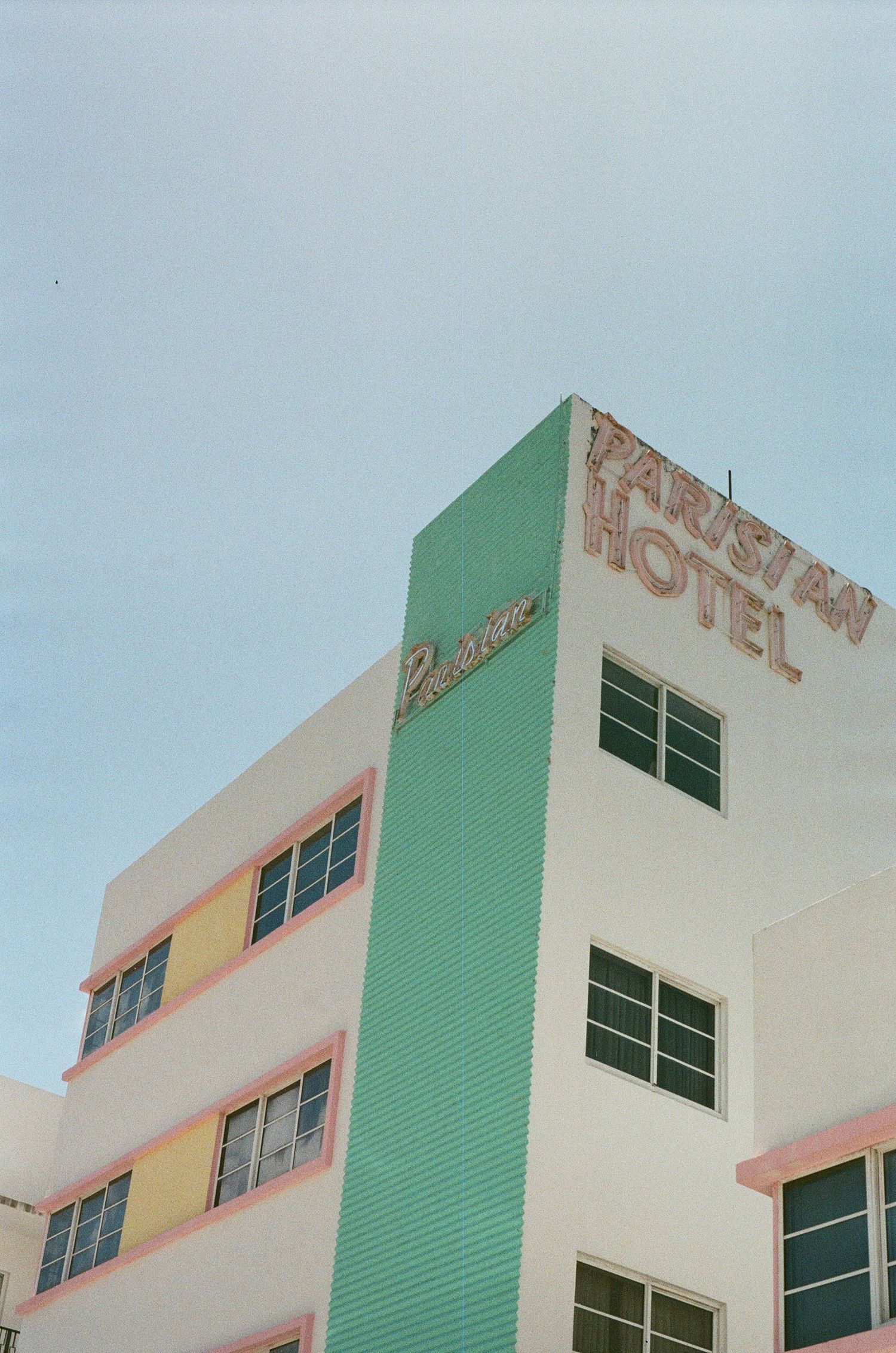 Pastel Art Deco Parisian Hotel facade with mint green tower and pink accents under clear blue sky in Miami Beach.