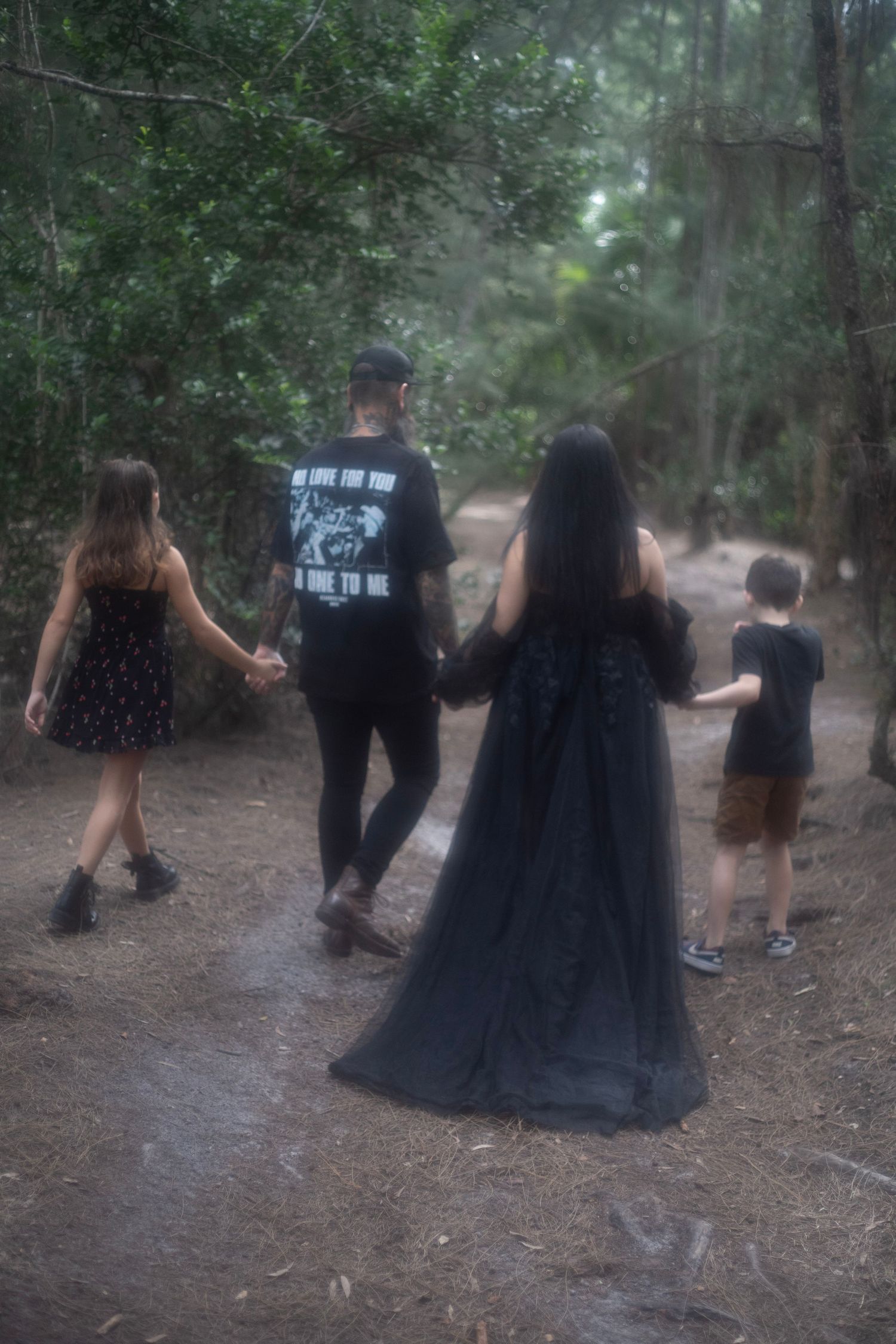 Family of four walking hand-in-hand along a forest path during a maternity photo session.