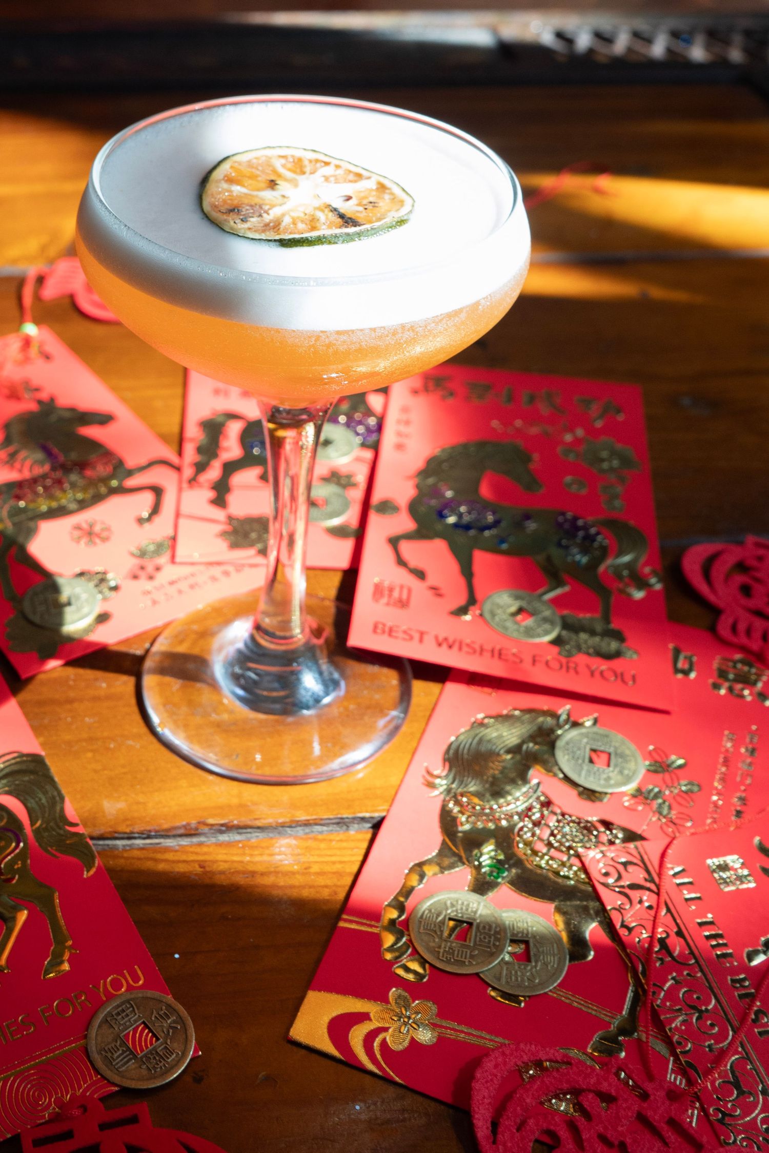 Elegant cocktail garnished with citrus slice in coupe glass surrounded by Chinese New Year red envelopes.