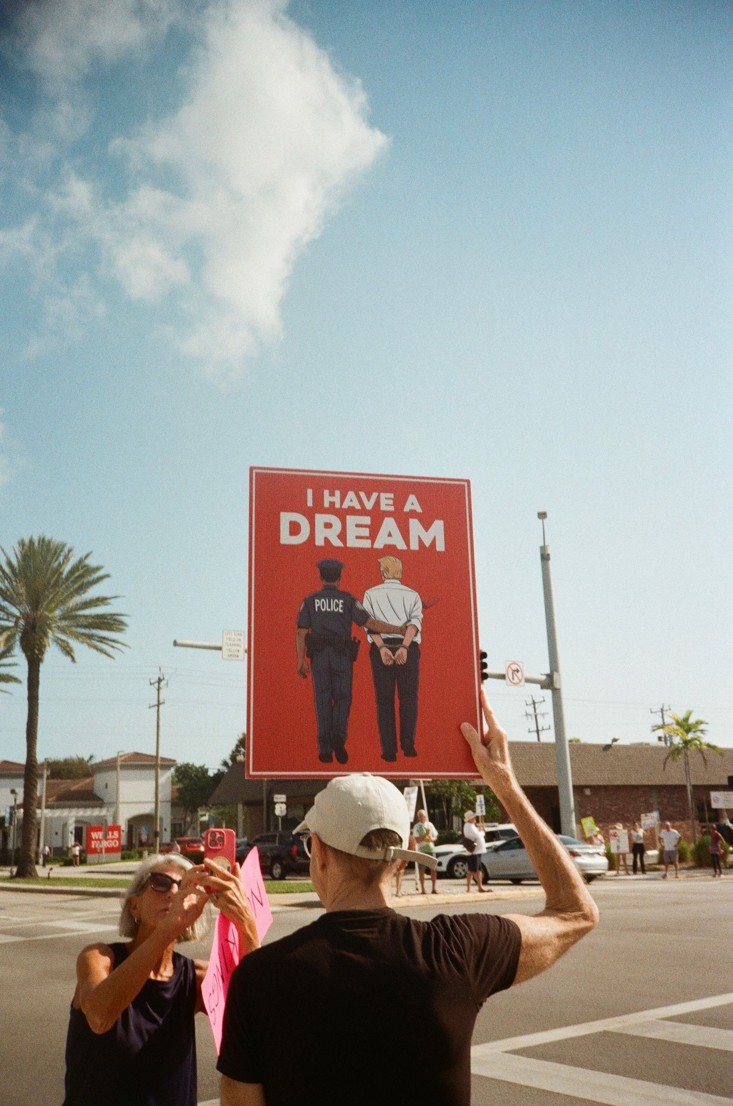 A protester holds a red sign reading I Have A Dream showing a police officer and handcuffed figure.