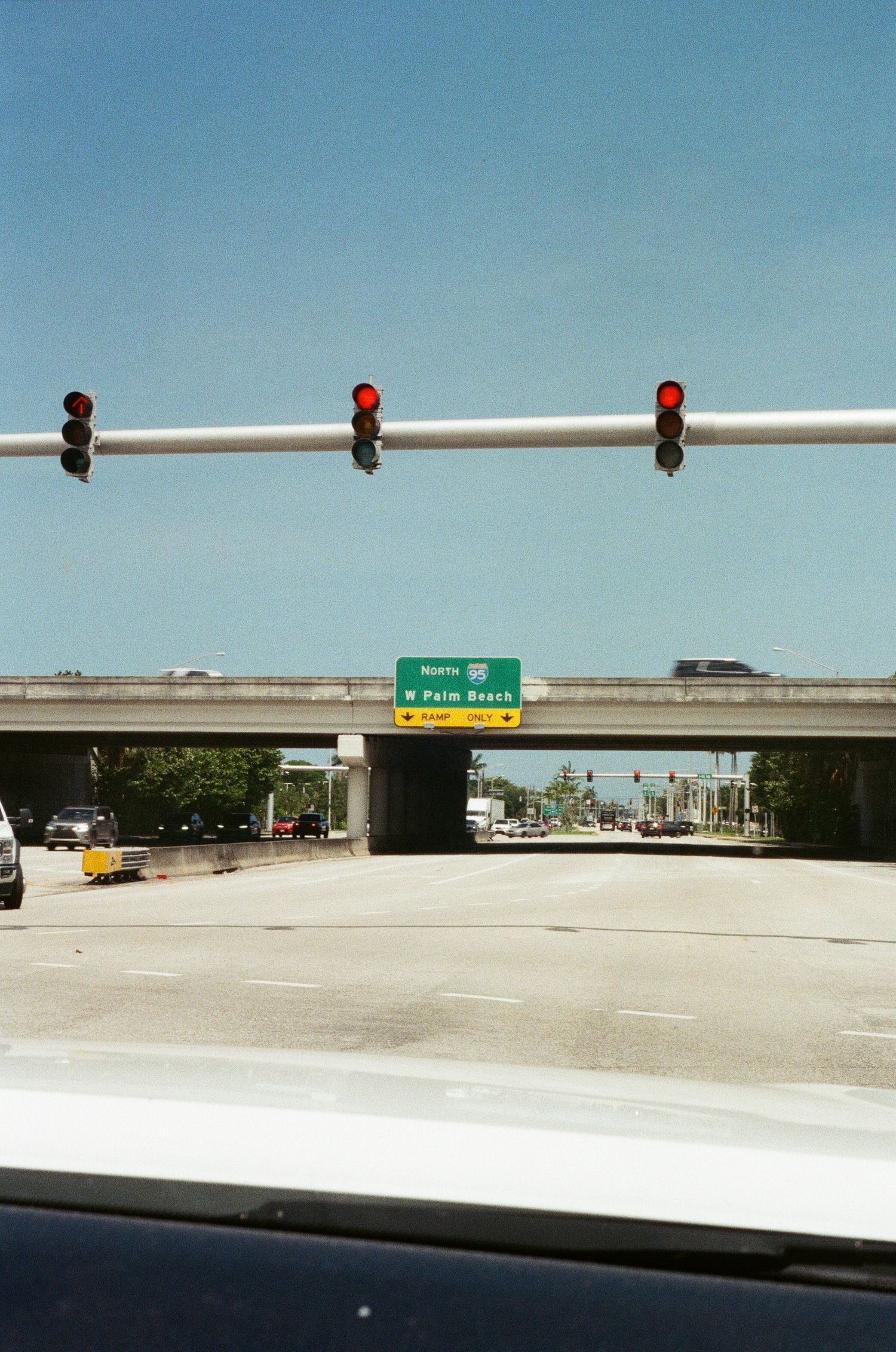 Red traffic lights hang over a multi-lane intersection with a green highway sign directing toward N Palm Beach.