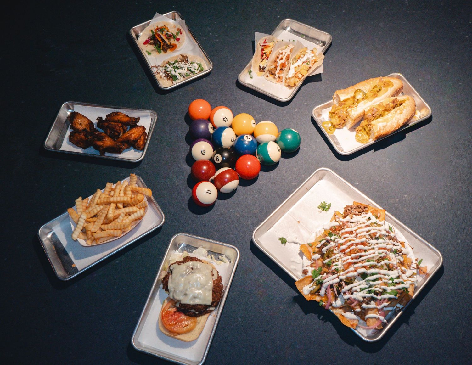 Overhead view of game night food spread with fries, wings, burger, nachos, and billiard balls.