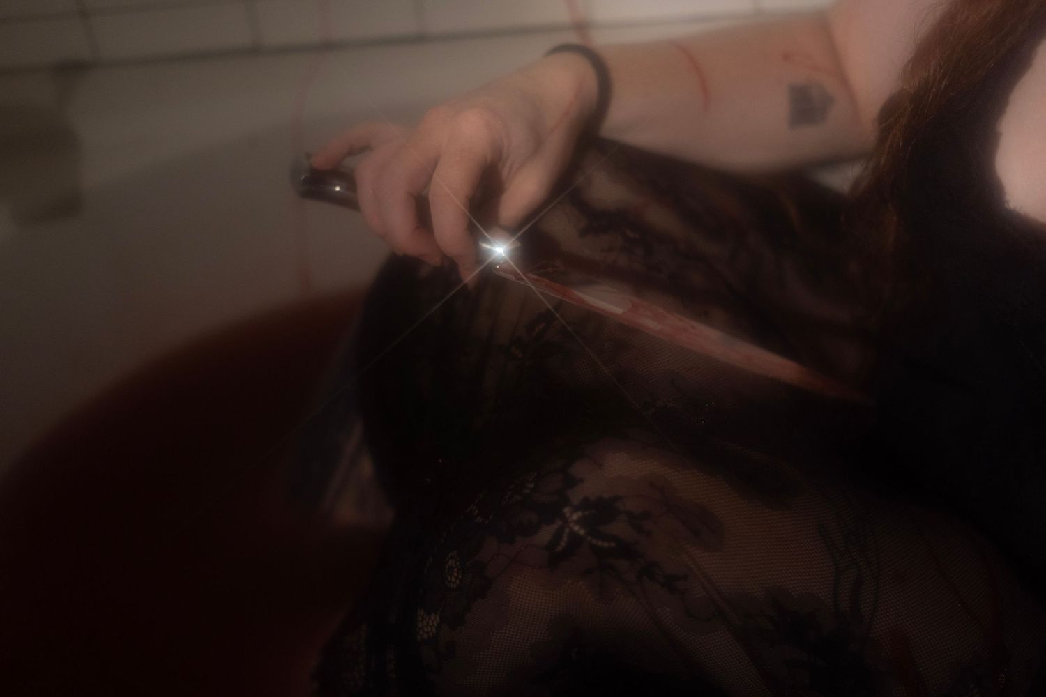 Person holding a knife while submerged in dark red liquid in a bathtub.