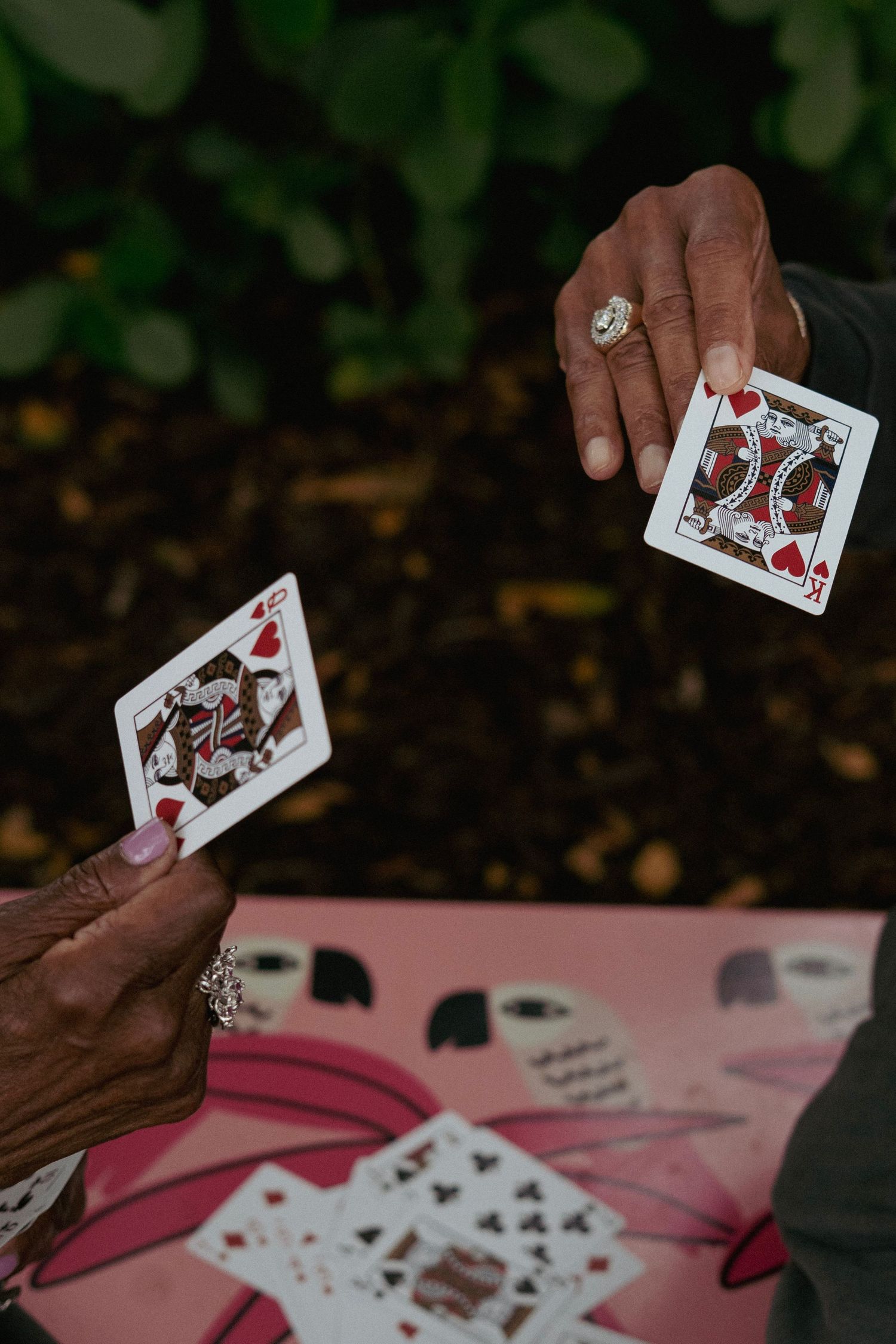 Close-up of two hands holding King of Hearts playing cards over a decorative card table.