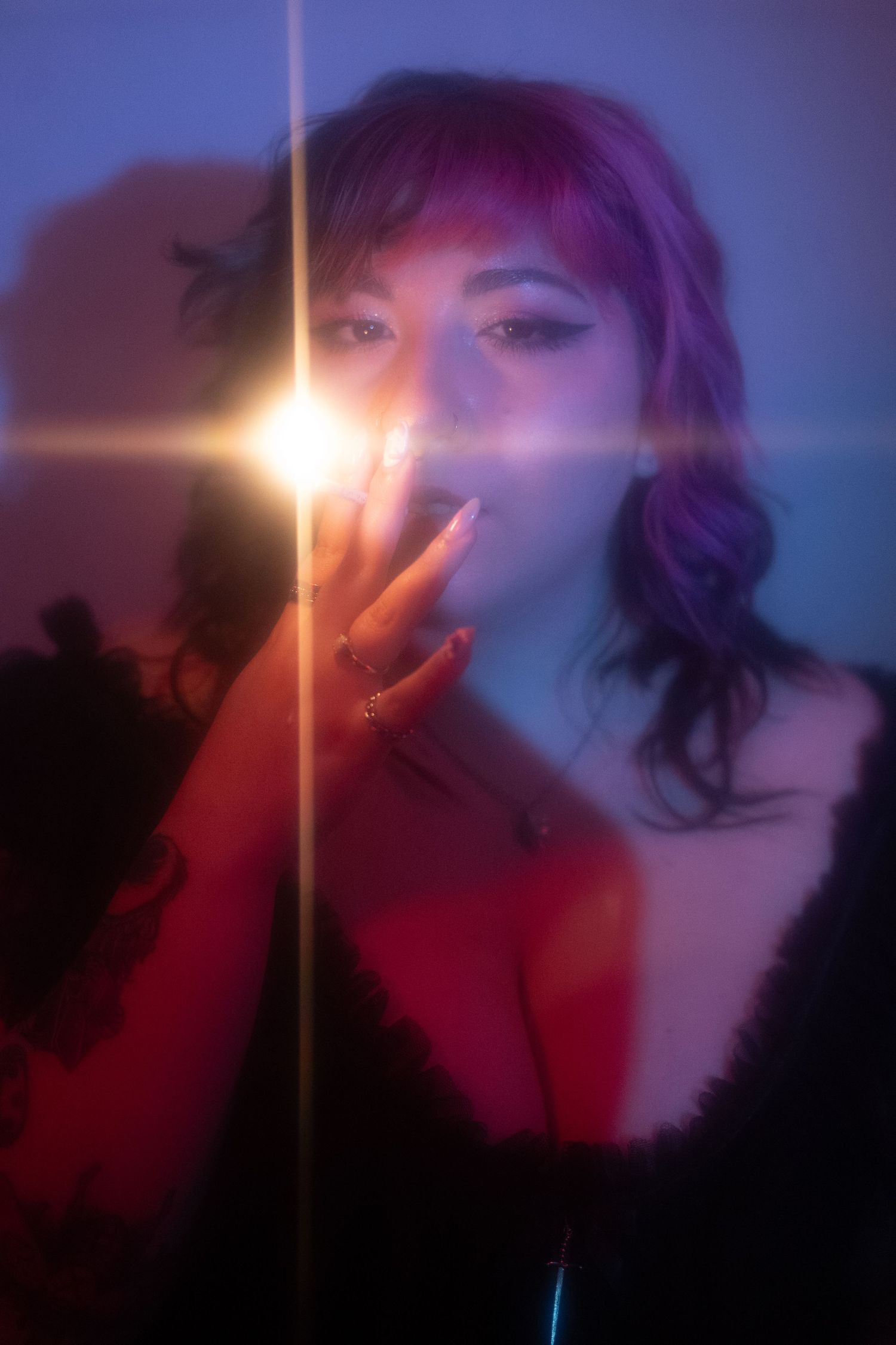 Woman with purple hair holding a light source behind glass with colorful bokeh effects.