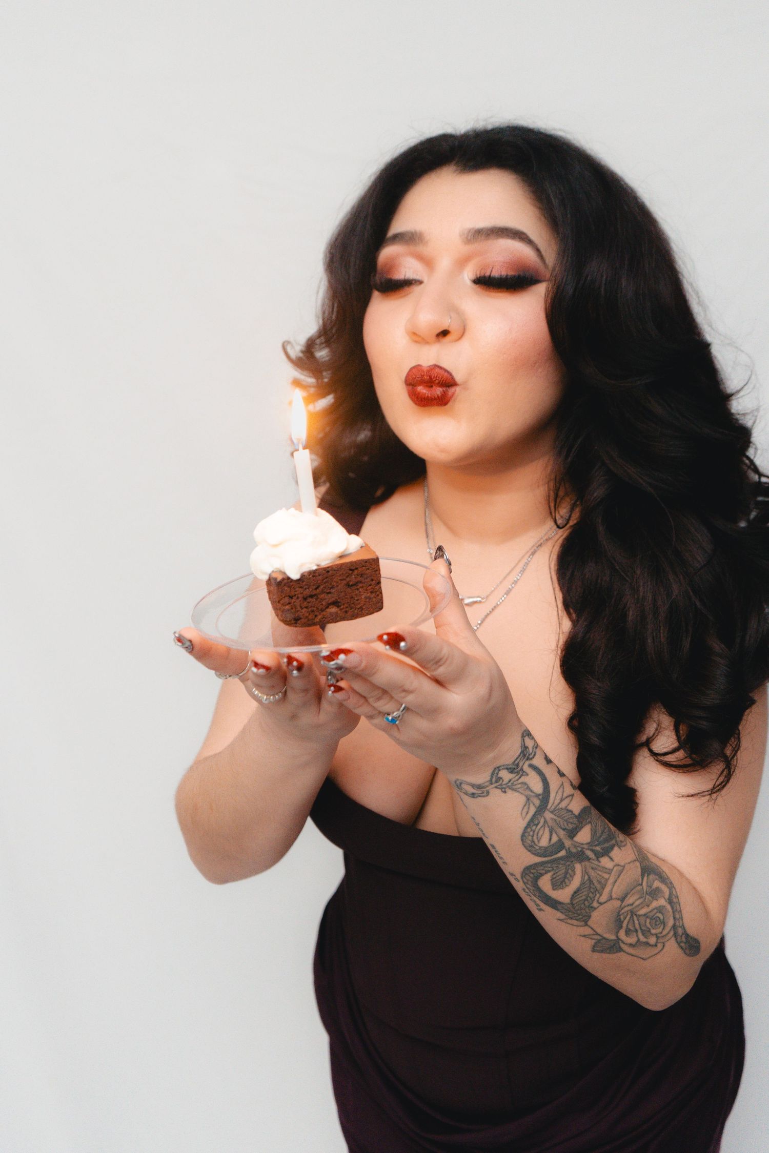 Woman with tattoos blowing out sparkler candle on birthday cupcake with white frosting.