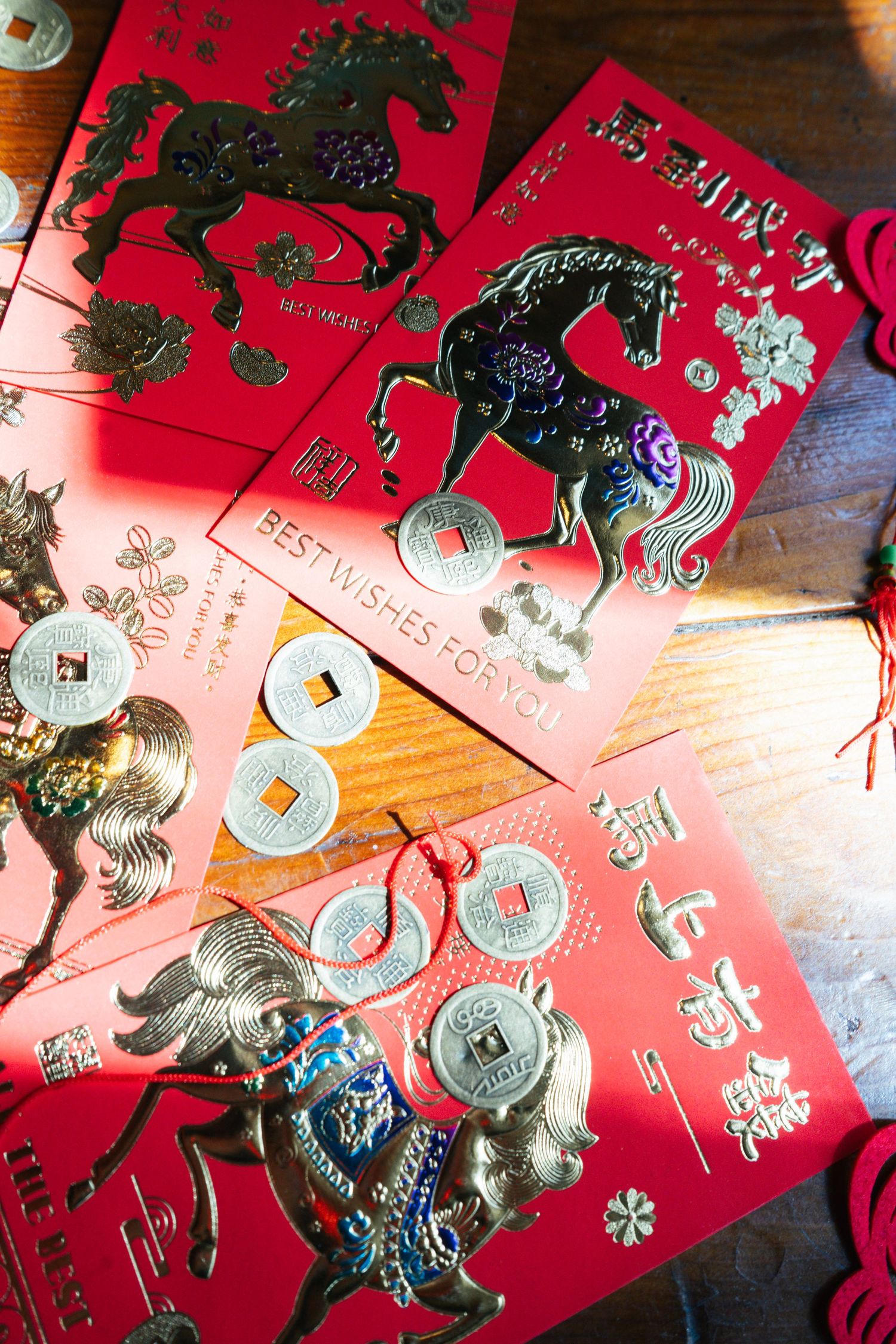 Chinese New Year red envelopes with gold horse designs and lucky coins arranged on wooden surface.