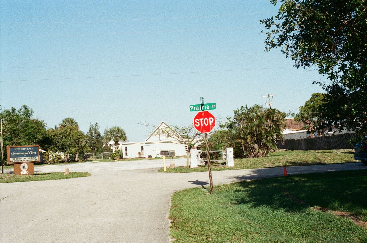 A stop sign at a quiet suburban intersection with a white building and palm trees in the background.