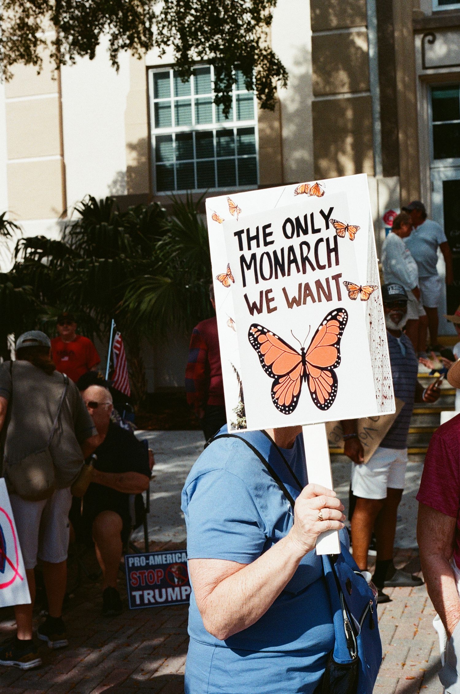 A protester holds a sign reading The Only Monarch We Want featuring a monarch butterfly illustration.
