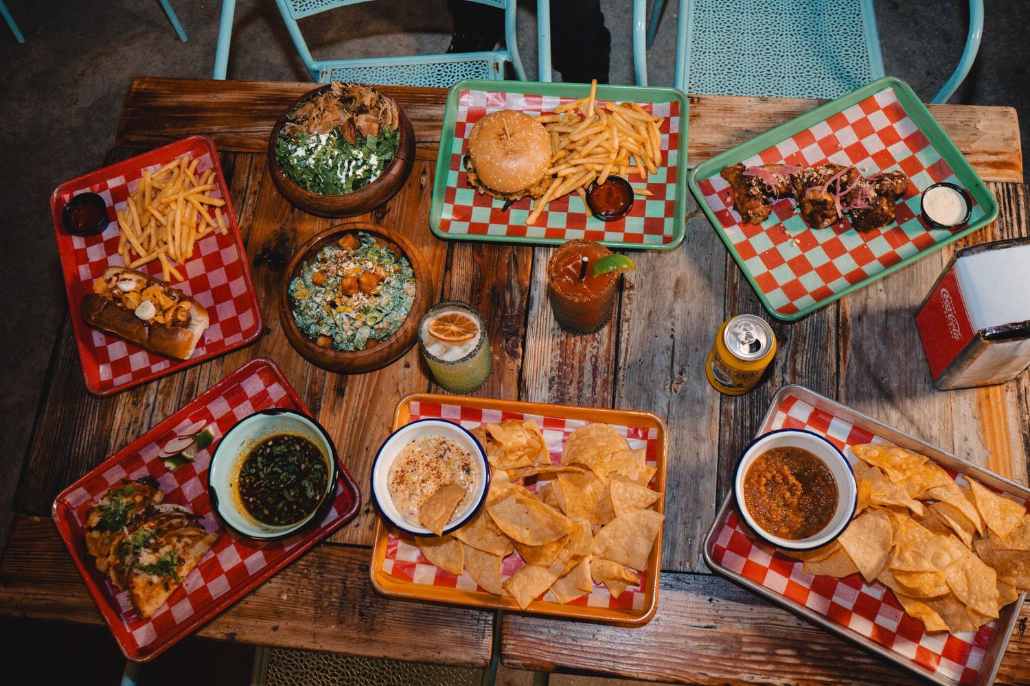 An overhead view of a spread of Mexican dishes including burritos, tacos, chips, and sides on a wooden table.