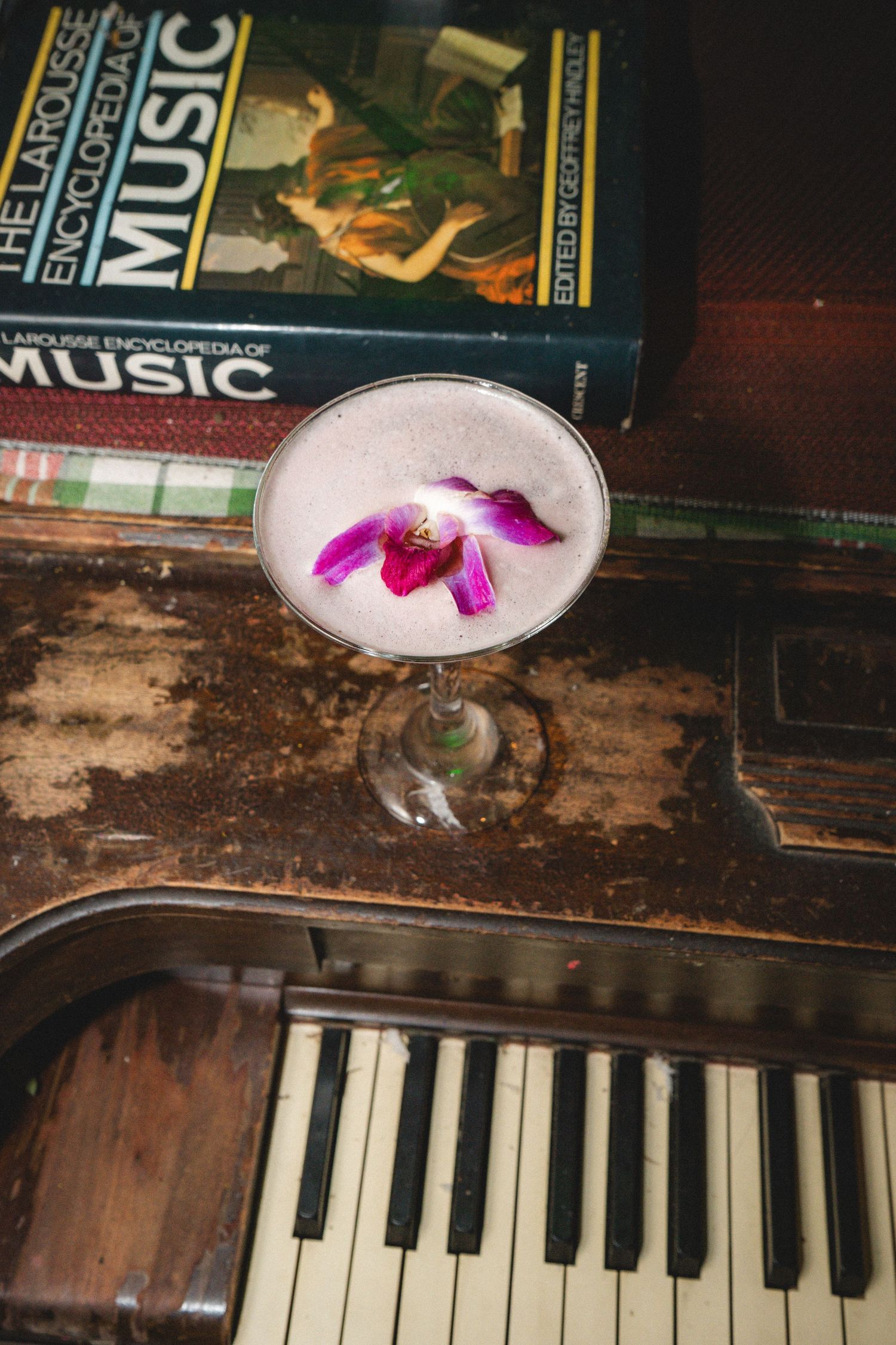 Elegant cocktail garnished with purple orchid flower served in coupe glass on vintage piano keys with music books.