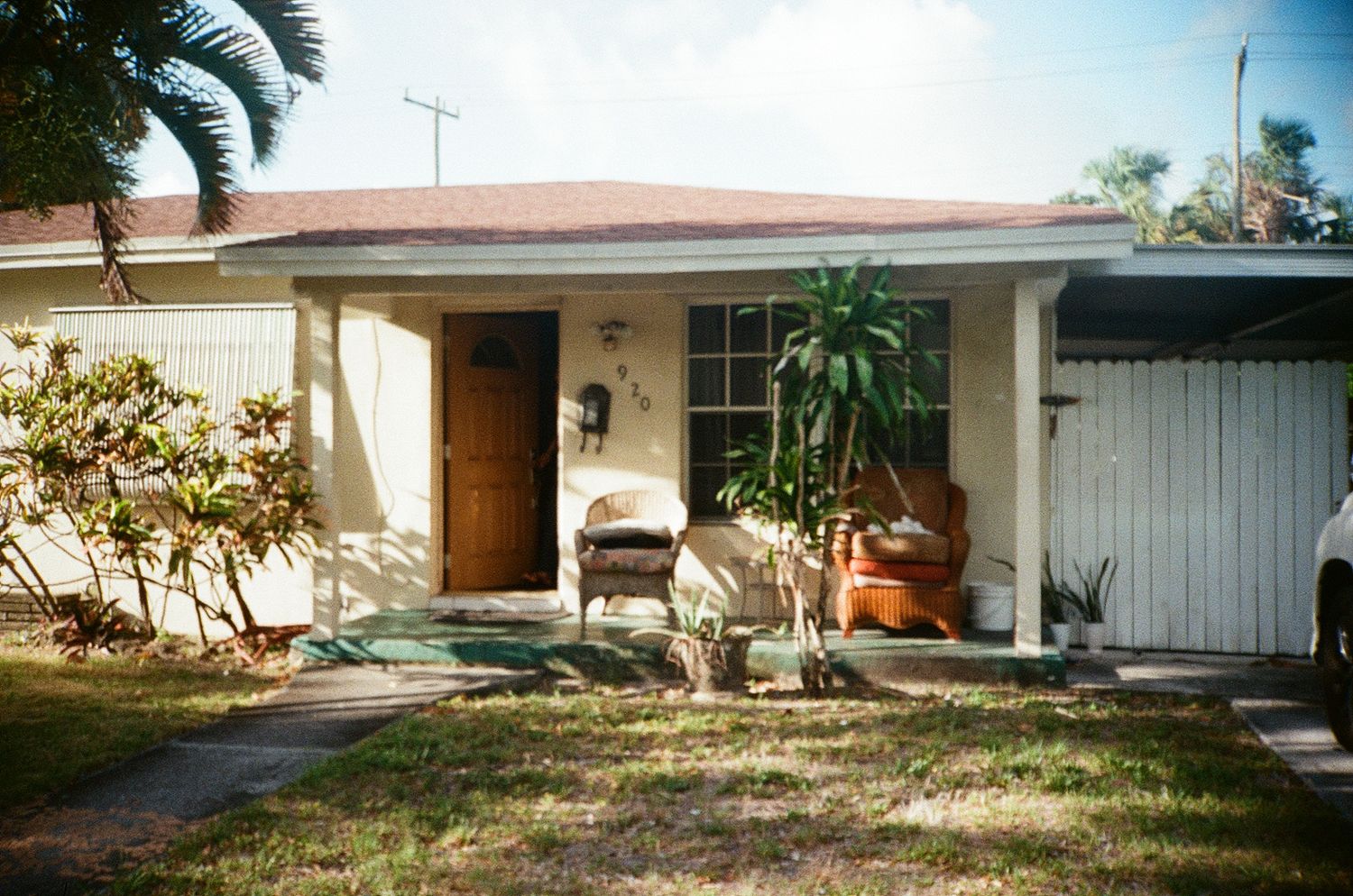 Small Florida ranch-style home with covered front porch, potted plants, wooden door, and lush green lawn.