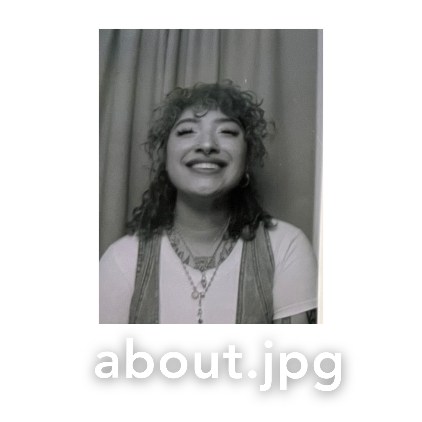 Black and white photo of a young woman with curly hair smiling broadly, wearing a necklace and casual top.