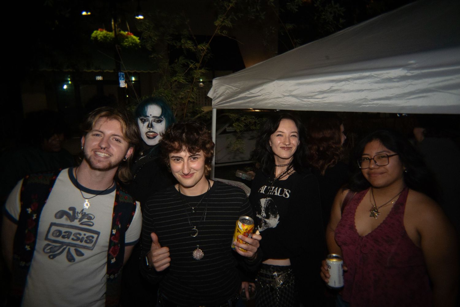 Group of five friends posing together at a nighttime outdoor party, one wearing KISS-style face paint.