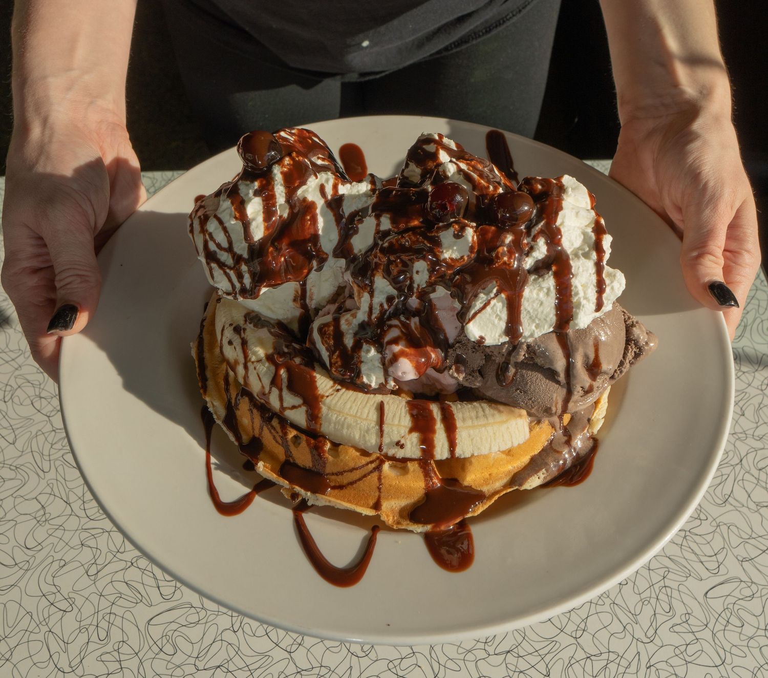 Decadent pancake stack topped with whipped cream, banana, and chocolate sauce on a white plate.