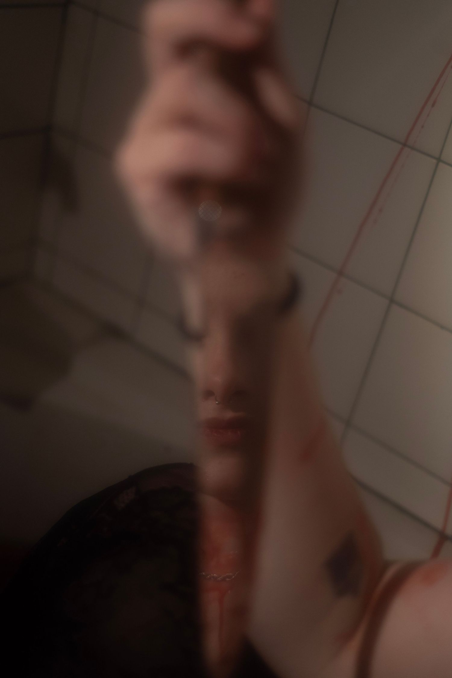 Blurry self-portrait of person holding phone in dimly lit bathroom.