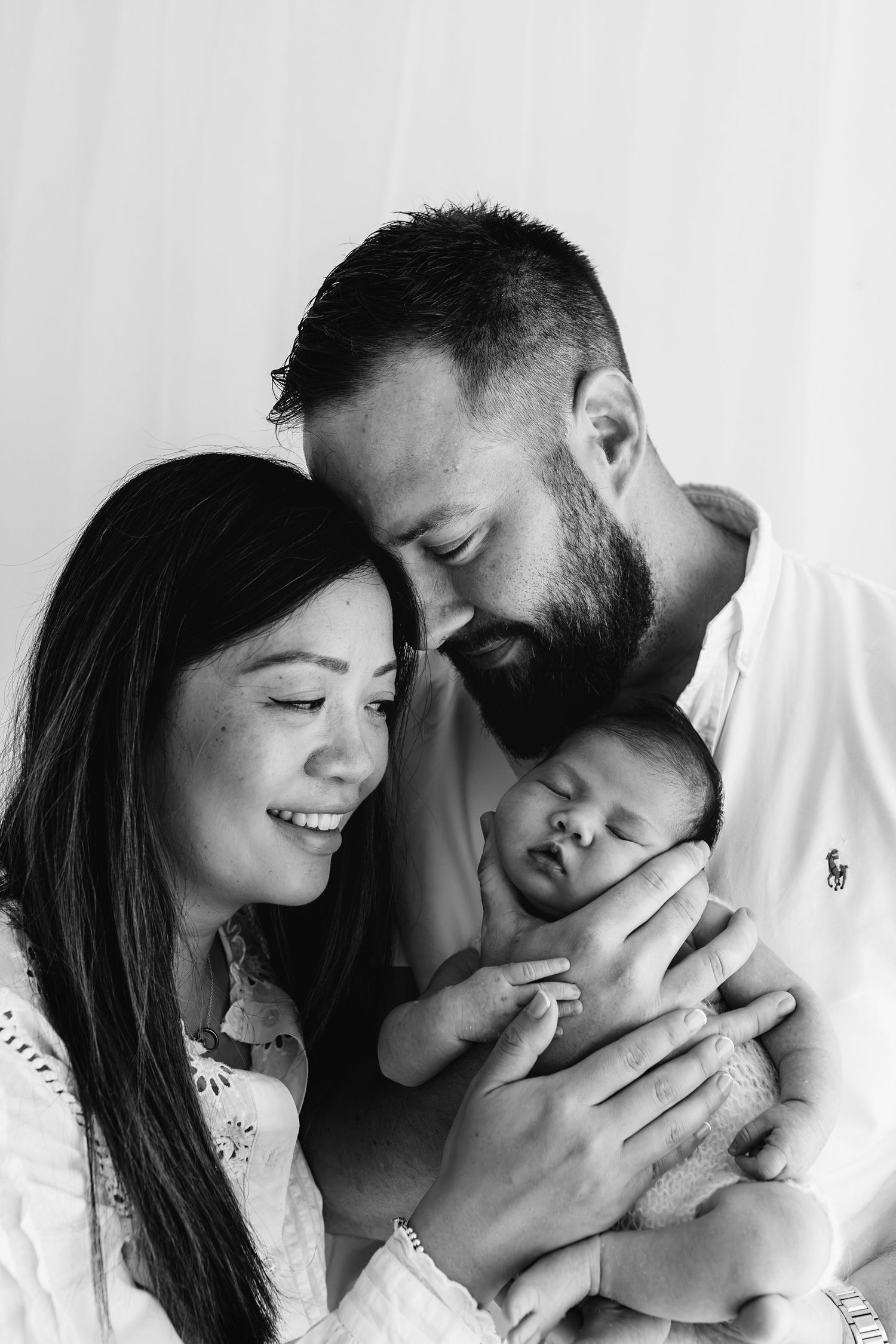 Black and white portrait of parents tenderly holding their sleeping newborn baby close.