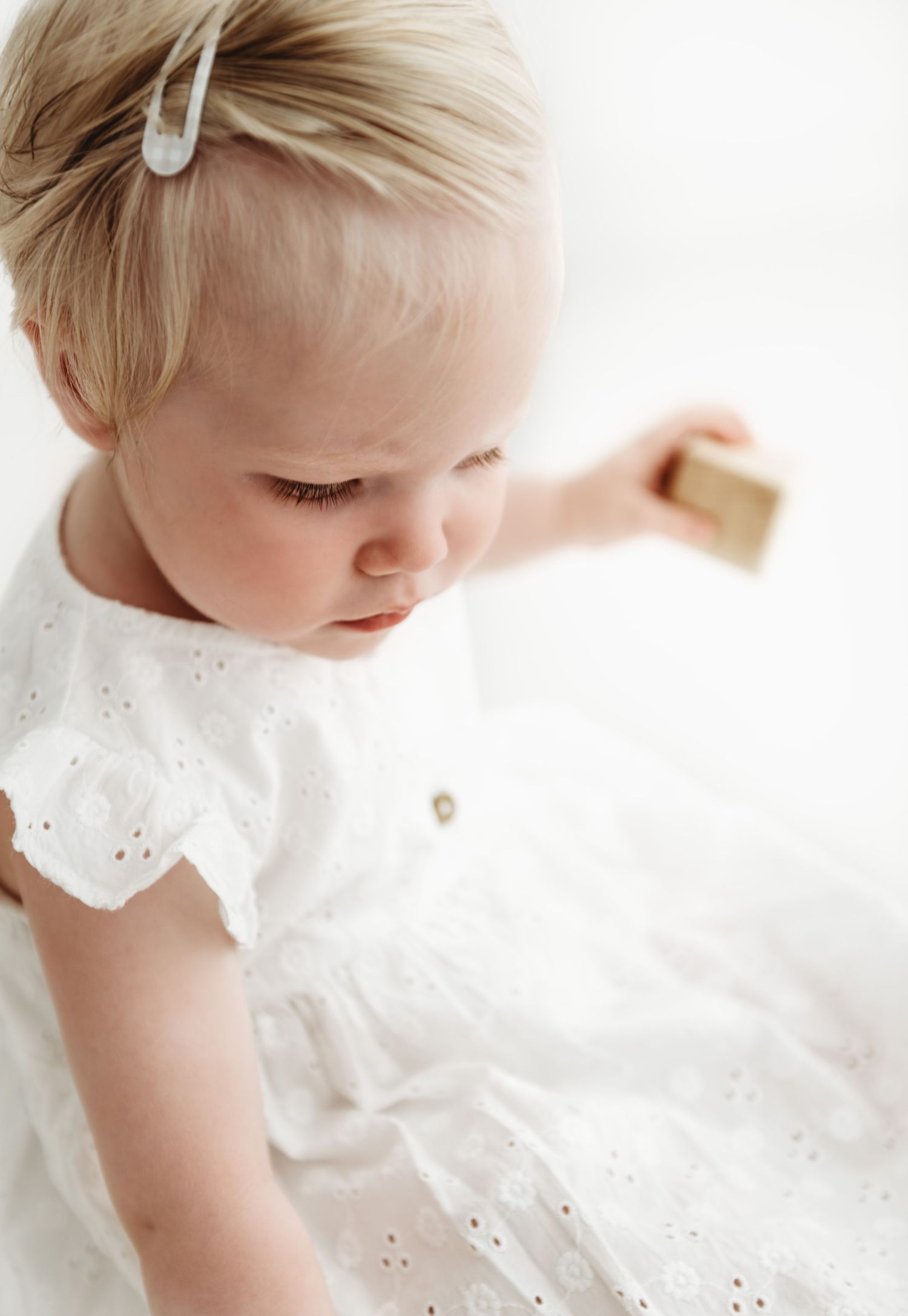 A series of delicate close-up photos showing a baby wearing a white eyelet lace dress gazing downward.