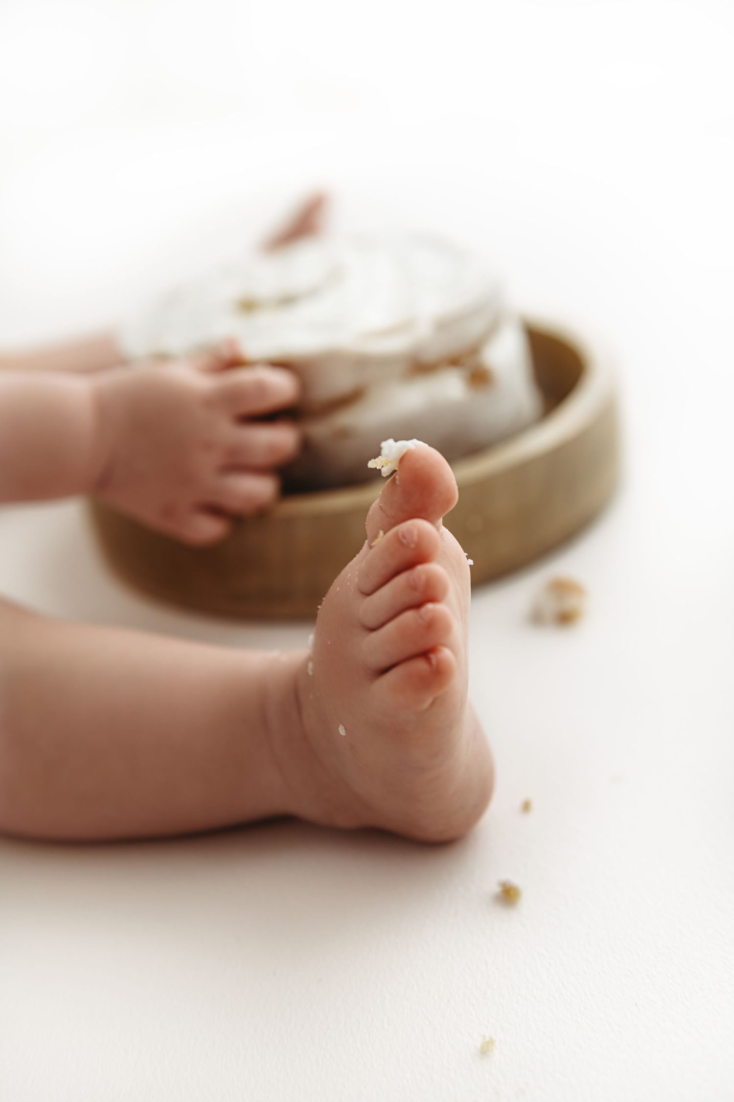 Close-up of tiny baby feet next to a bowl with crumbs scattered on a white surface.
