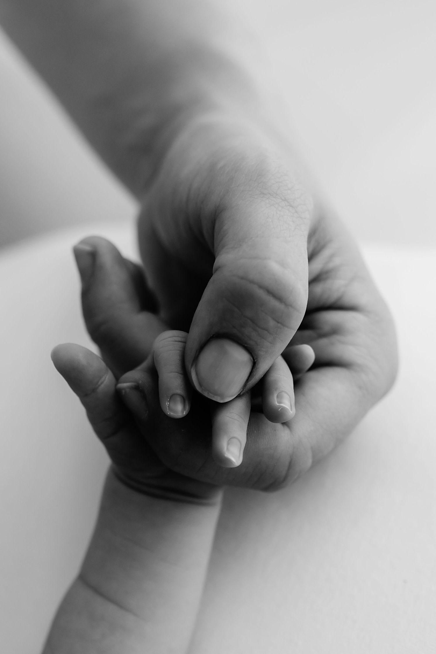 Black and white close-up of an adult hand gently holding a newborn baby's tiny hand.